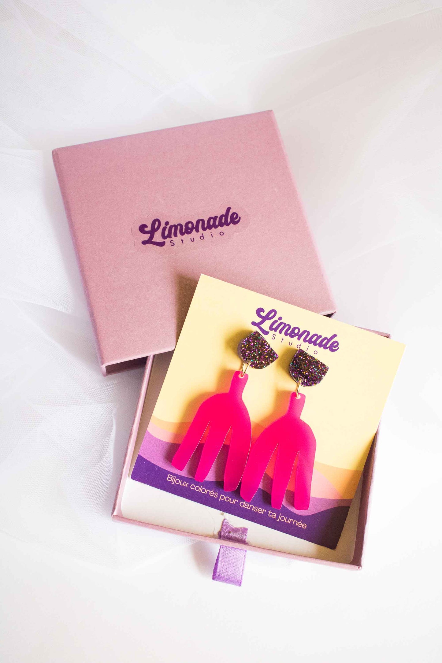 Boucles d'oreilles pendantes fuchsia Limonade Studio dans leur boîte cadeau rose, cartonnette visible, vue de dessus