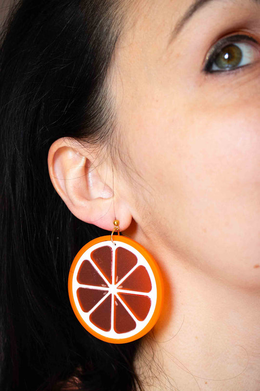Boucle d'oreille pendante tranche d'orange en acrylique fait main, puce plaquée or, bijou coloré Limonade Studio, portée en gros plan sur oreille droite