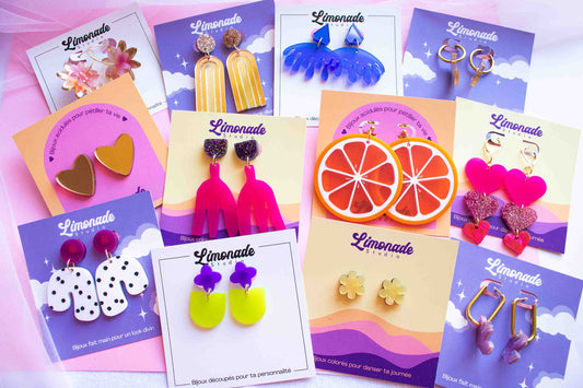 Vue de dessus d'une collection de boucles d'oreilles acryliques colorées Limonade Studio sur fond rose — fleurs jaune, orange, cœurs et vagues