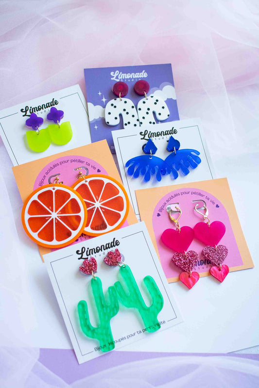 Flat lay de boucles d'oreilles acryliques colorées Limonade Studio — cœurs, fleurs, étoiles et vagues sur cartes de présentation variées