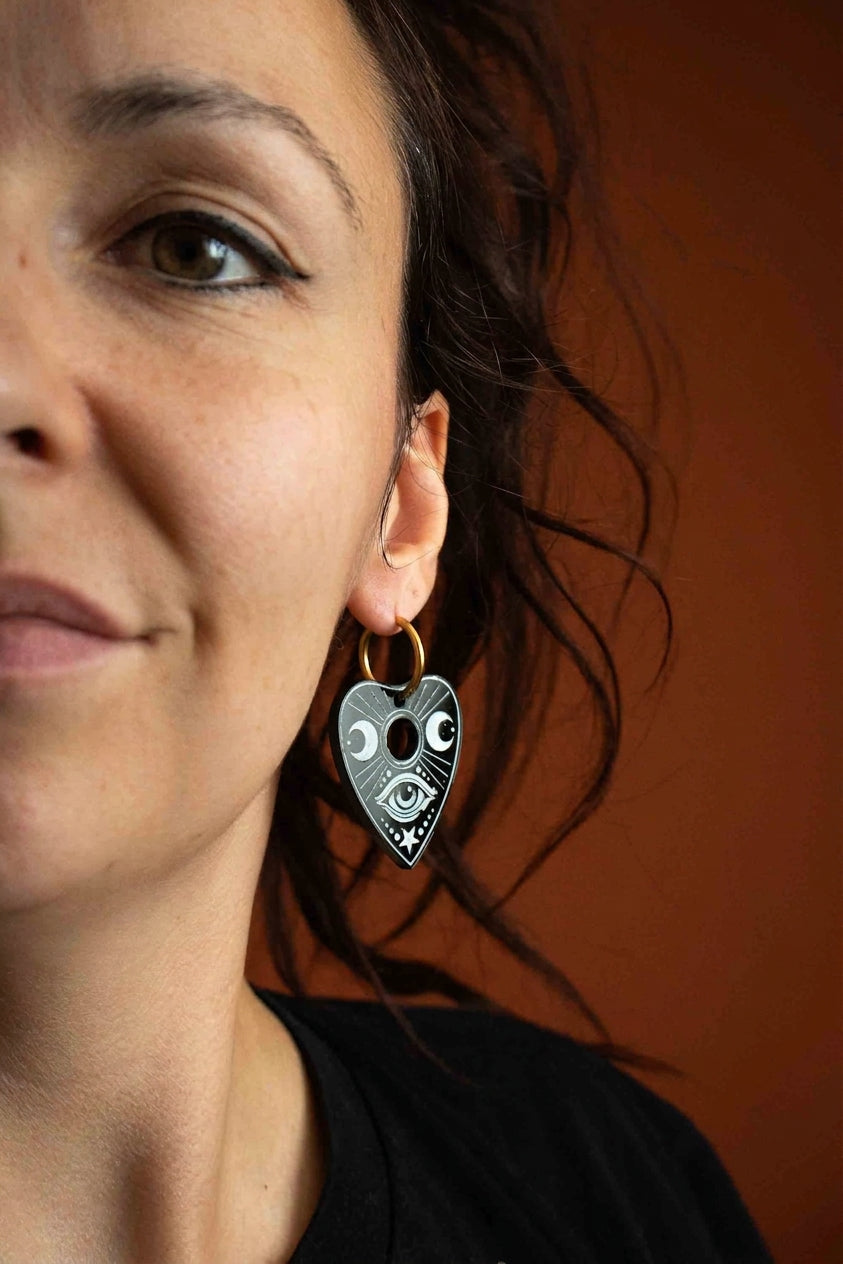 Femme portant une planchette Ouija noire gravée de blanc suspendue à un petit anneau doré