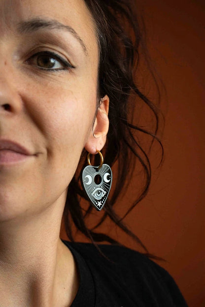 Femme portant une planchette Ouija noire gravée de blanc suspendue à un petit anneau doré