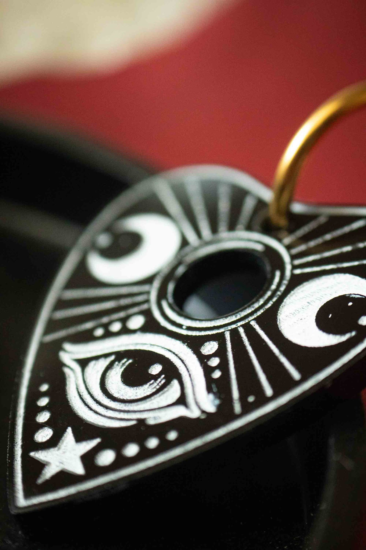Gros plan sur l’œil mystique et les lunes gravés en blanc dans une planchette Ouija noire