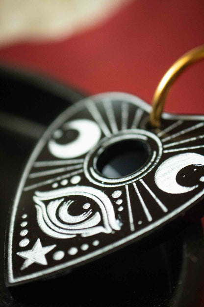 Gros plan sur l’œil mystique et les lunes gravés en blanc dans une planchette Ouija noire