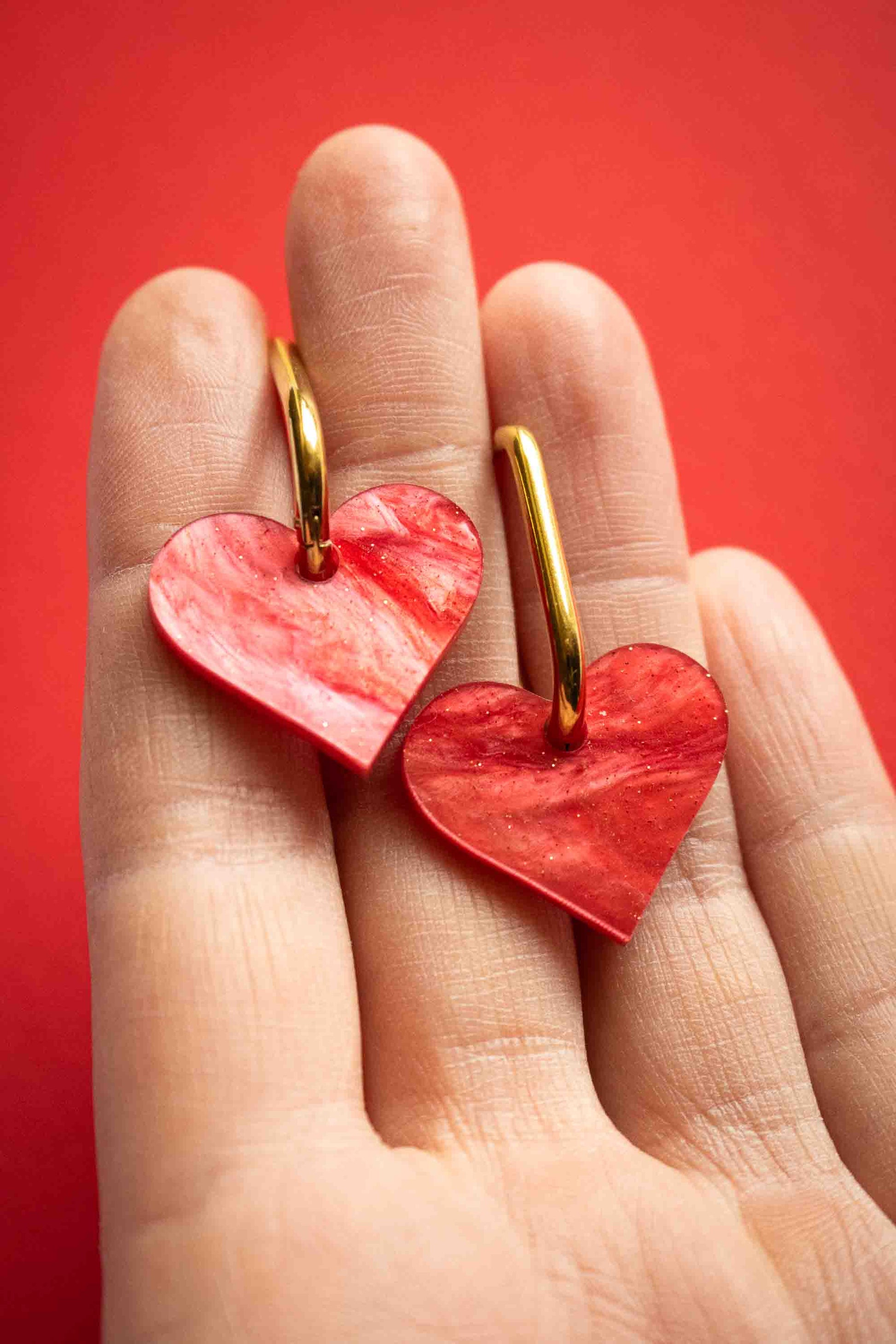 Boucles d'oreilles cœur rouge marbré acrylique fait main Limonade Studio, tenues en main sur fond rouge vif, bijou coloré cadeau femme