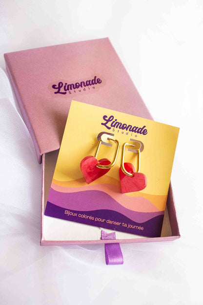 Gros plan packaging Limonade Studio, boîte cadeau violette avec boucles cœur rouge acrylique sur cartonnette, bijou fantaisie artisanal prêt à offrir