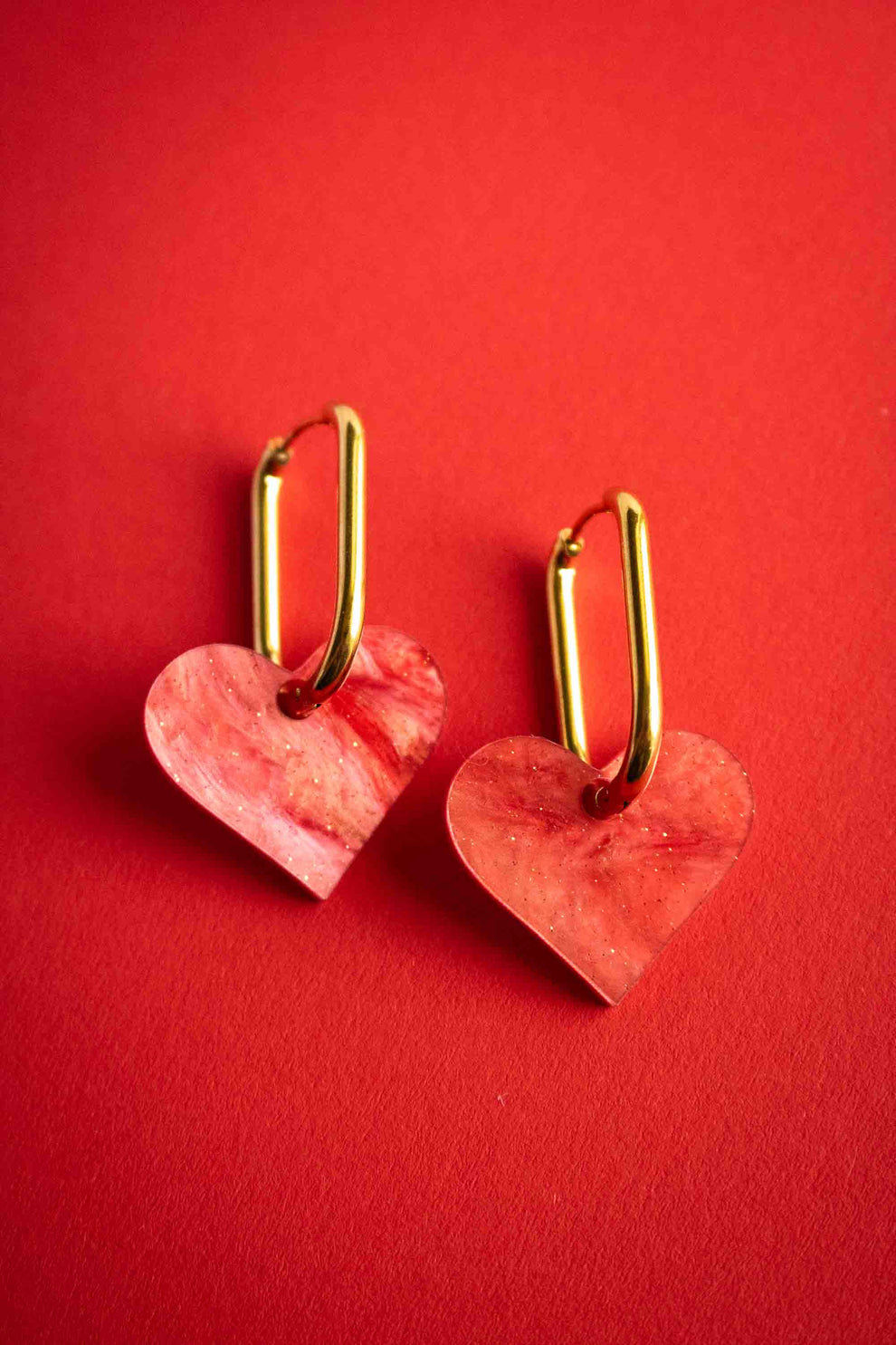 Boucles d'oreilles cœur rouge en acrylique marbré pailleté, anneaux ovales plaqués or 18 carats. Limonade Studio.