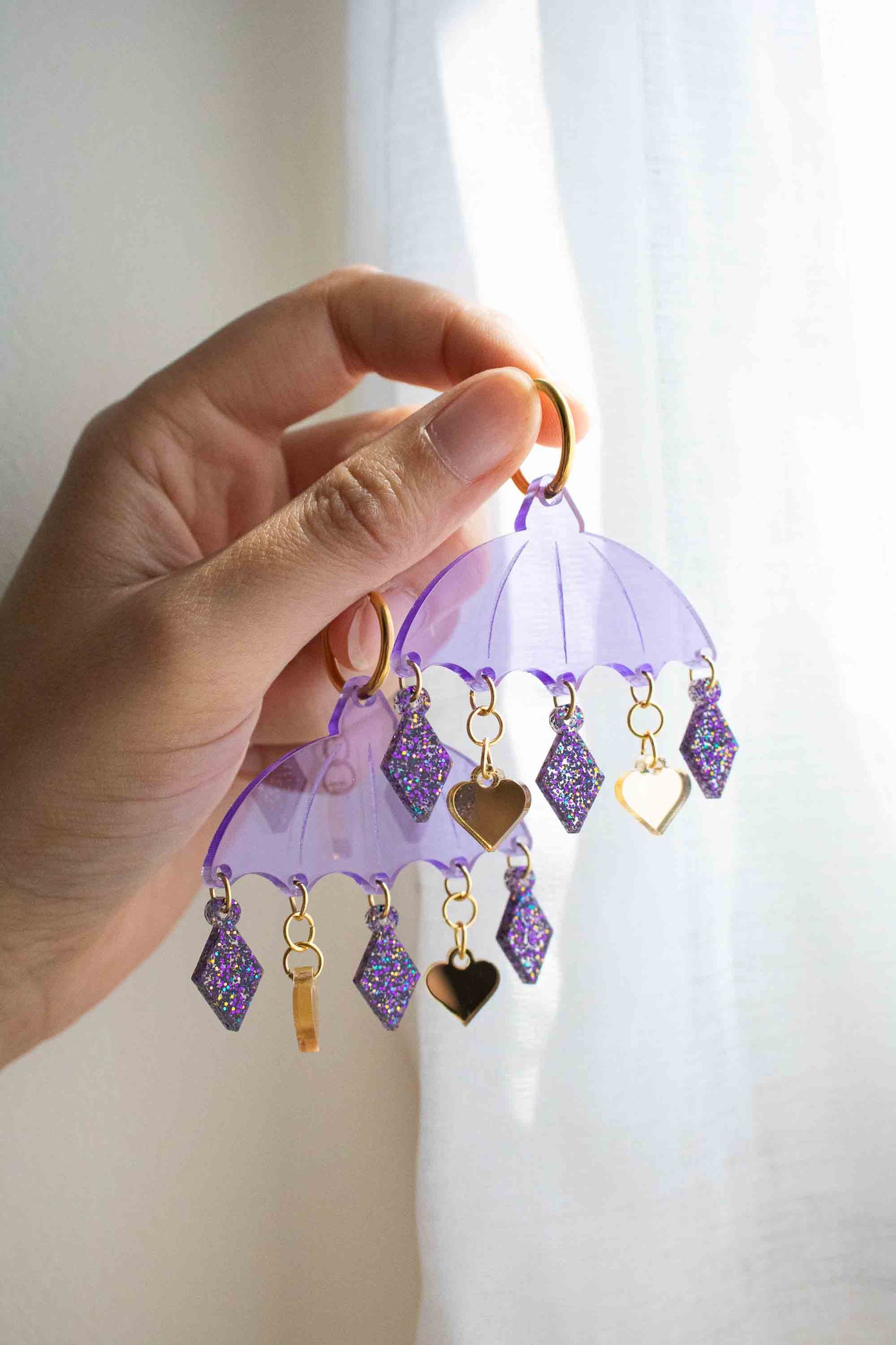 Boucles d'oreilles violettes en acrylique decoupe laser, bijou colore fait main Limonade Studio, portees dans la main avec anneaux dores et charms.