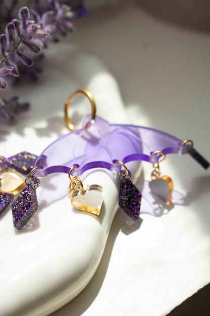 Boucles d'oreilles parapluie violettes en acrylique decoupe laser, bijou colore Limonade Studio, posees dans une coupelle avec lavande, gros plan sur les pampilles.
