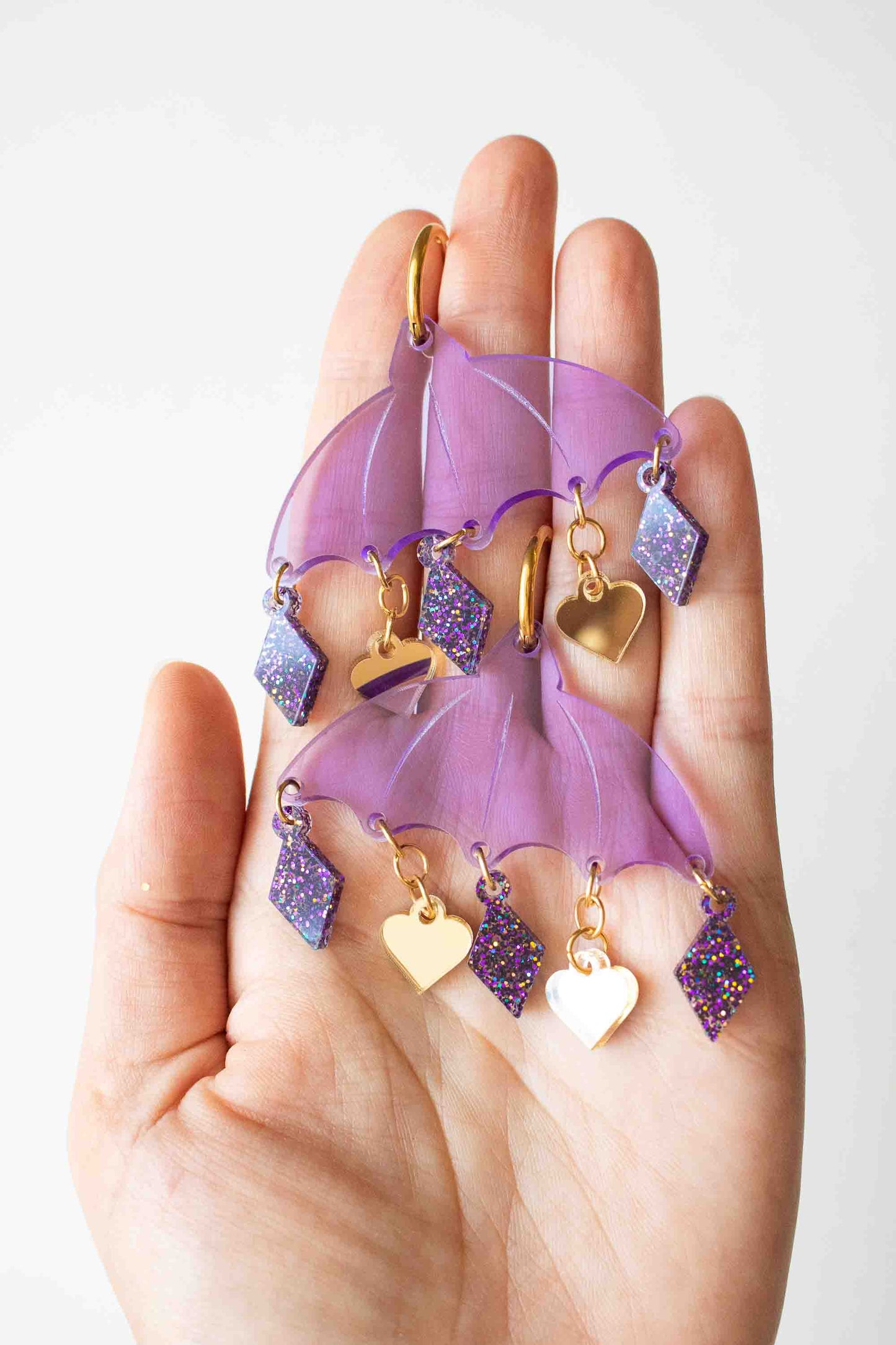 Boucles d'oreilles violettes en acrylique decoupe laser, bijou colore fait main Limonade Studio, bijoux poses dans la paume sur fond blanc.