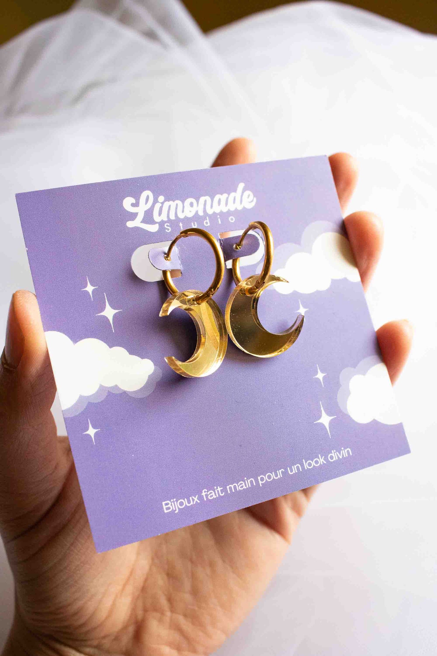 Paire de boucles huggies acier plaqué or avec lune acrylique miroir doré, cadeau femme fait main Limonade Studio, posées sur paume ouverte