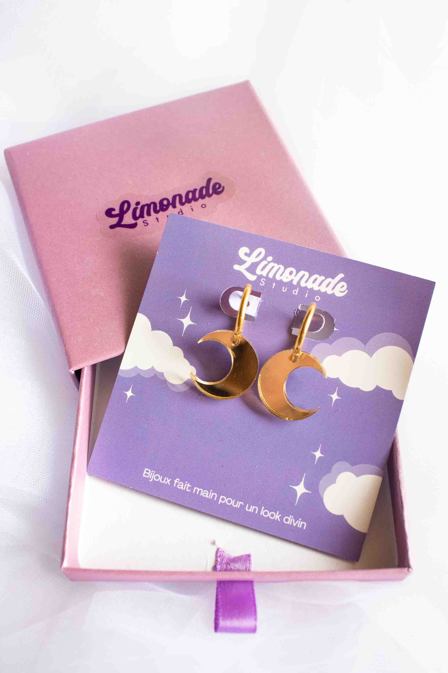 Boucles d'oreilles huggies lune dorée miroir, bijou artisanal fait main Limonade Studio, présentées dans leur boîte cadeau rose et cartonnette violette