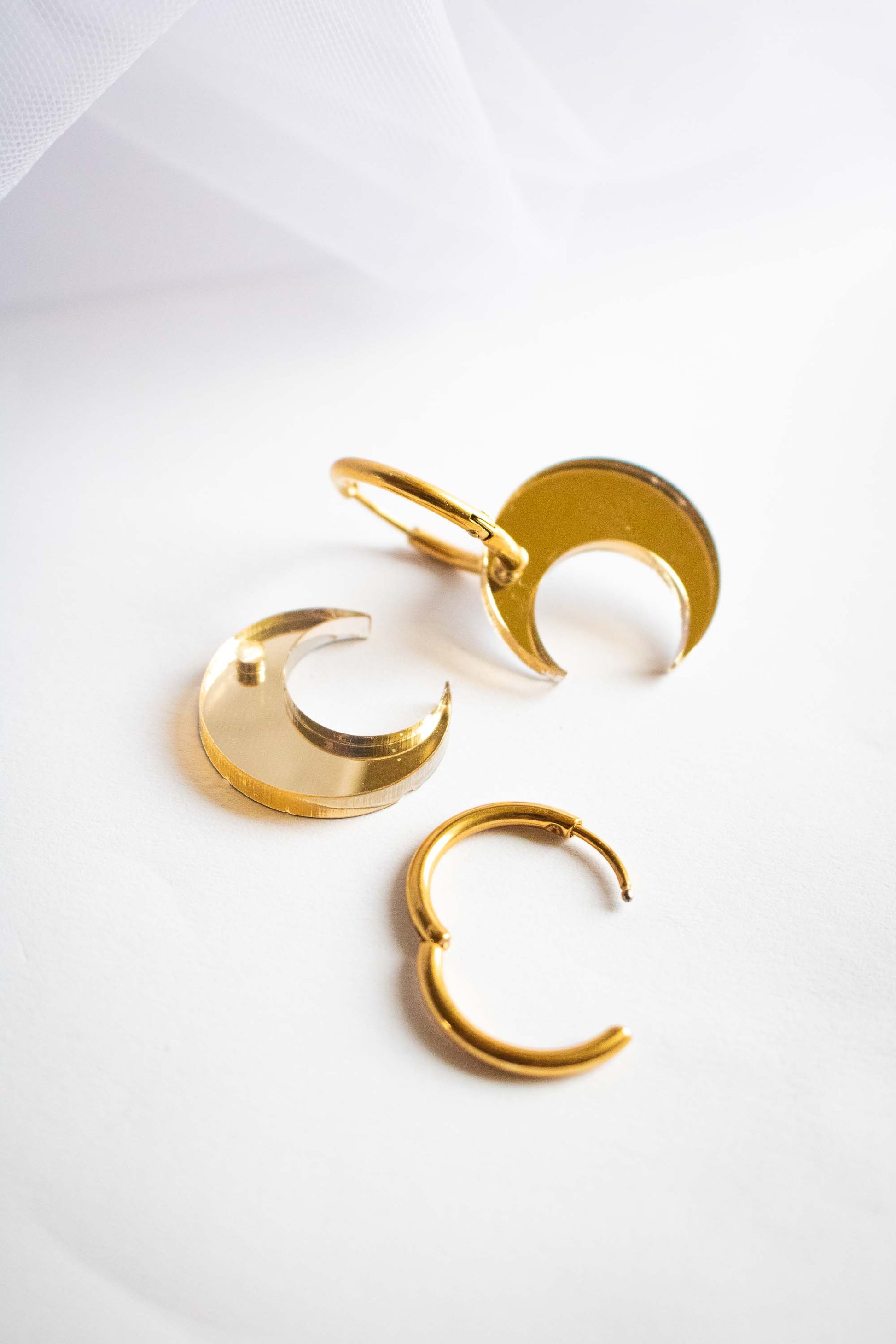 Composants dissociés des boucles huggies lune dorée miroir : anneaux acier plaqué or et pendentifs lune acrylique, fait main Limonade Studio, fond blanc