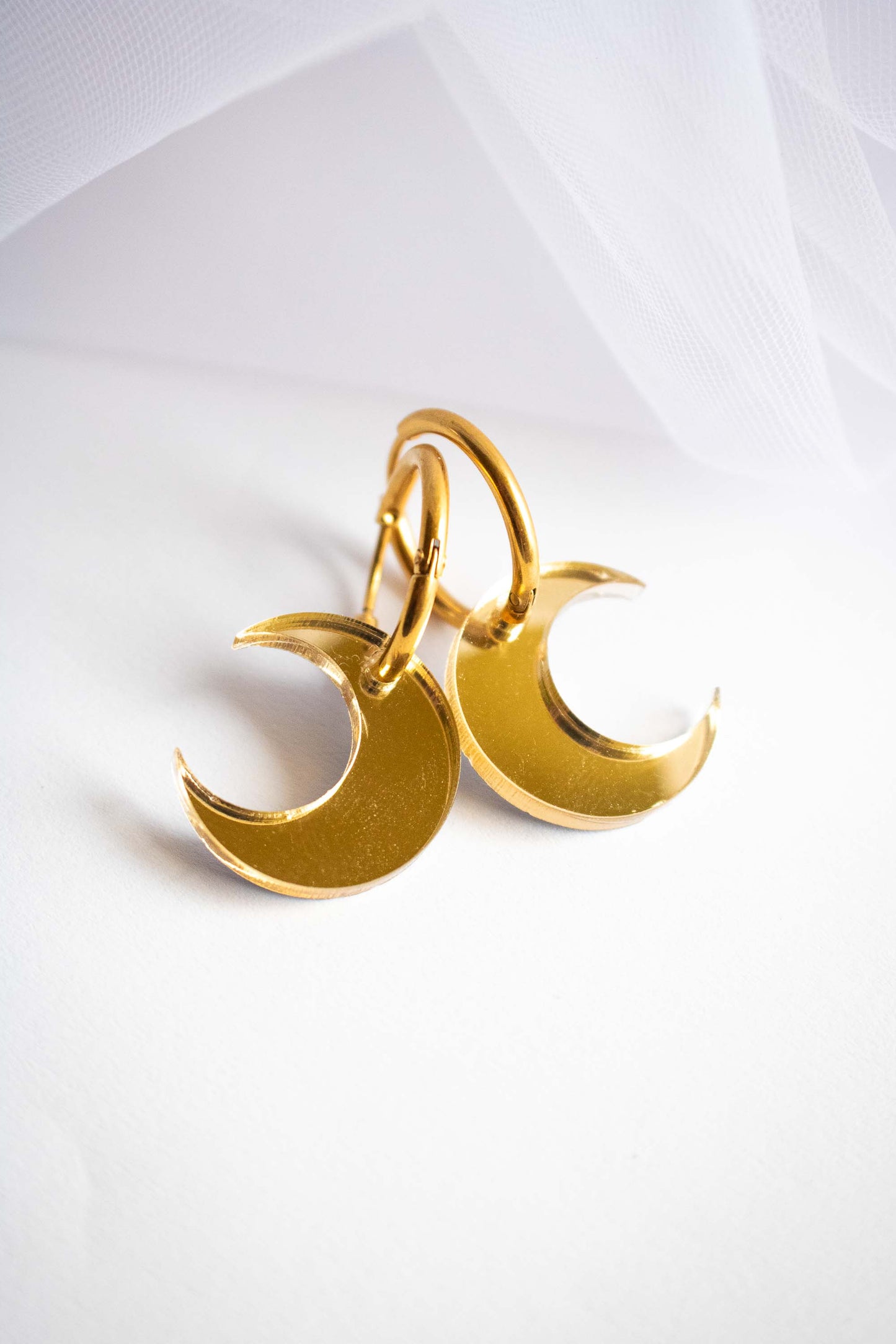 Boucles d'oreilles huggies acier plaqué or avec pendentif lune acrylique miroir doré, création fait main Limonade Studio, sur fond blanc