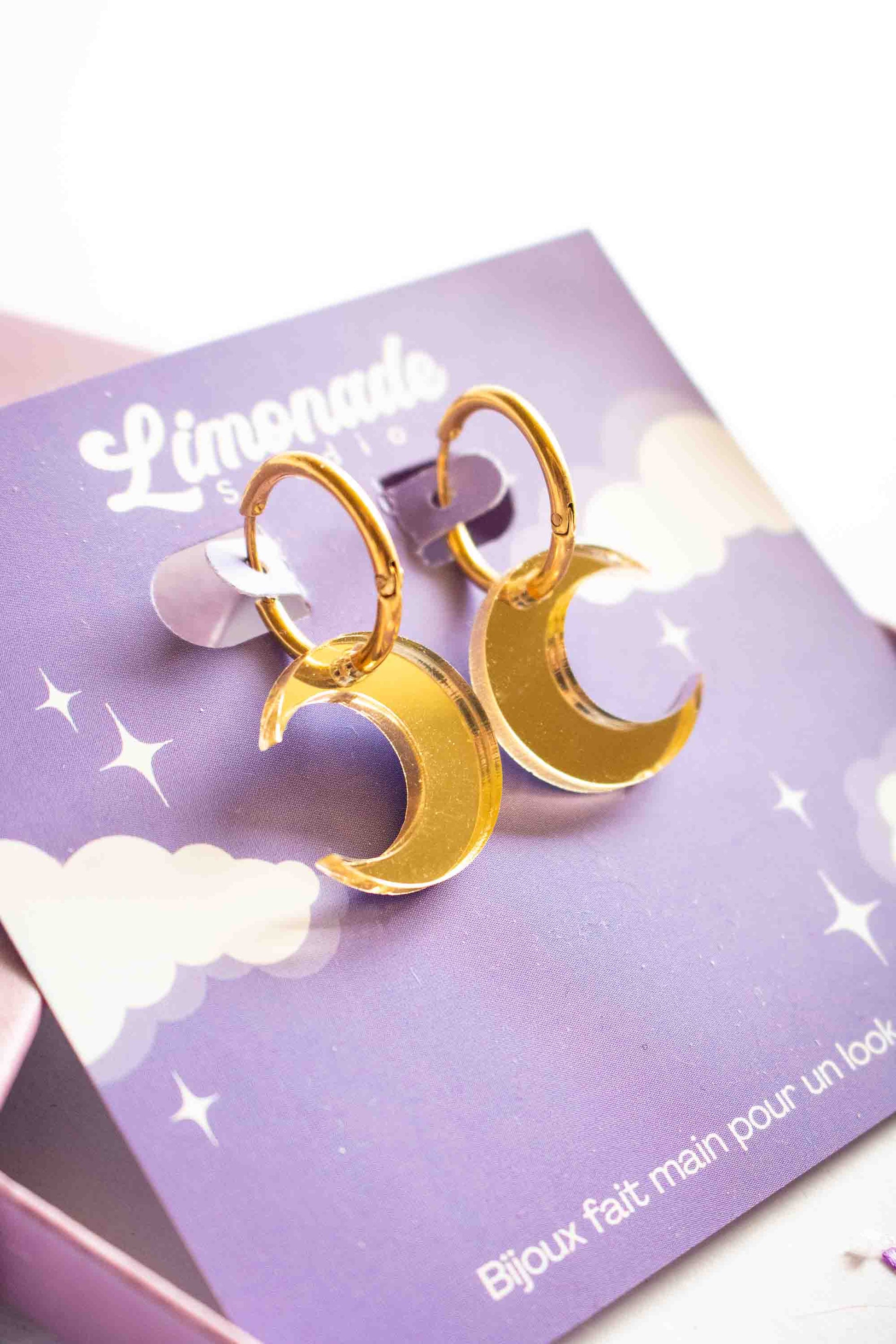 	Boucles huggies dorées avec lune acrylique miroir, vue trois quarts montrant l'épaisseur, bijou artisanal fait main Limonade Studio, fond blanc