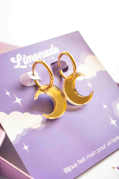 	Boucles huggies dorées avec lune acrylique miroir, vue trois quarts montrant l'épaisseur, bijou artisanal fait main Limonade Studio, fond blanc