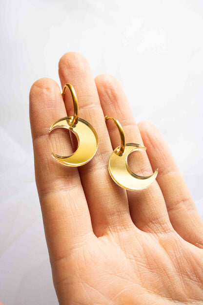 Paire de boucles huggies dorées avec lune acrylique miroir doré, bijou fantaisie fait main Limonade Studio, tenues sur paume ouverte face avant