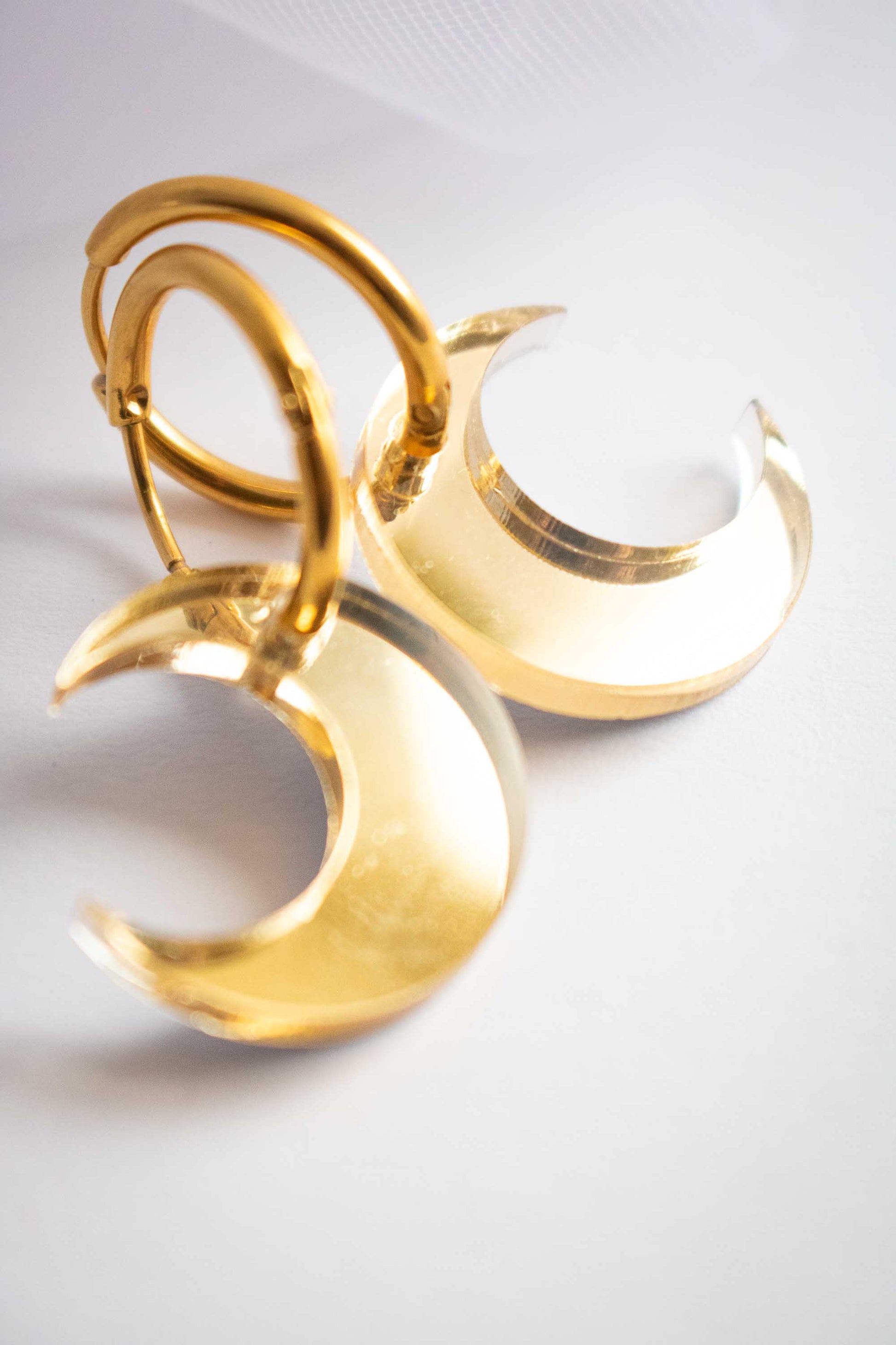 Boucles huggies dorées avec lune acrylique miroir, vue trois quarts montrant l'épaisseur, bijou artisanal fait main Limonade Studio, fond blanc