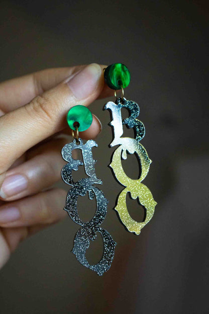 Boucles d’oreilles BOO en acrylique noir pailleté tenues en main