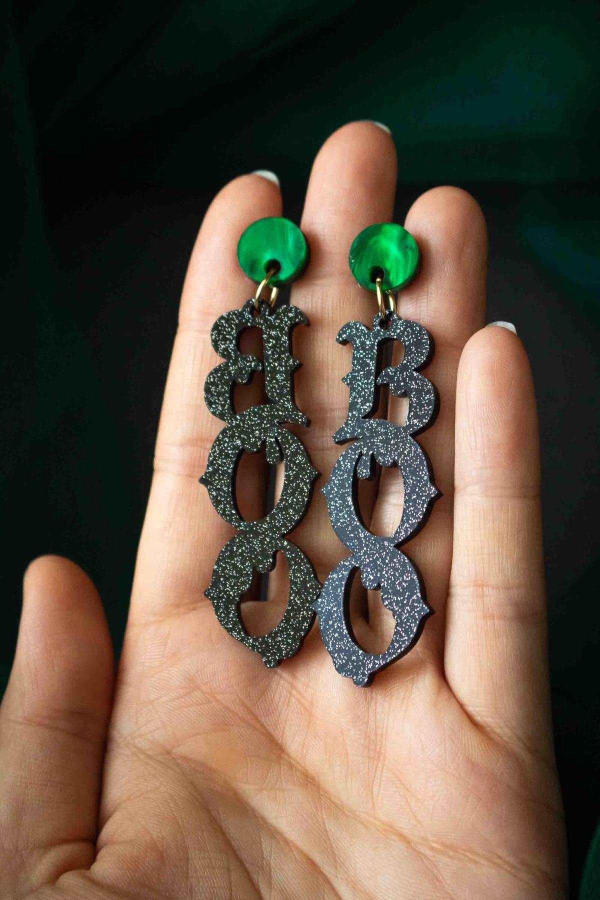 Boucles d’oreilles BOO halloween noires pailletées présentées dans une main