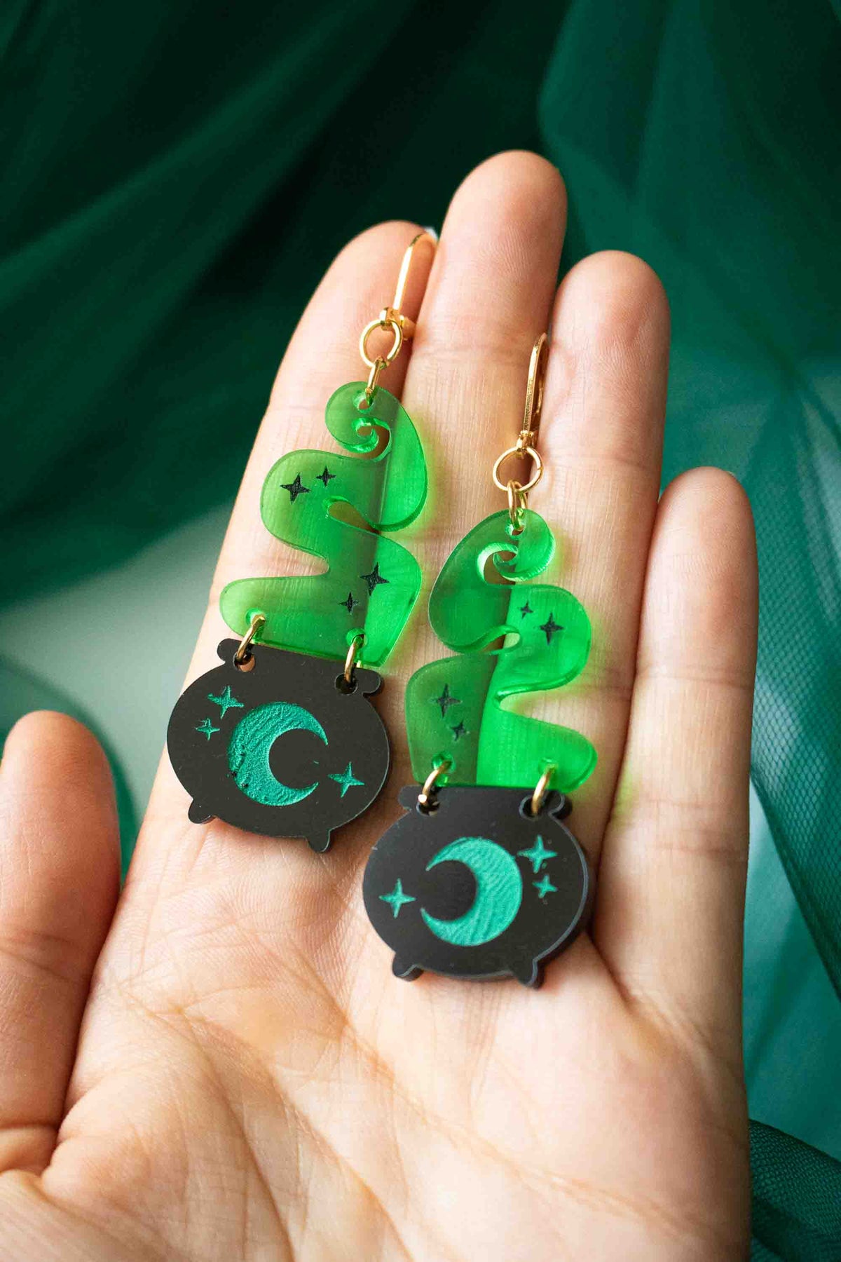 Paire de boucles d’oreilles chaudron noir et fumée verte présentée dans une main pour montrer sa taille