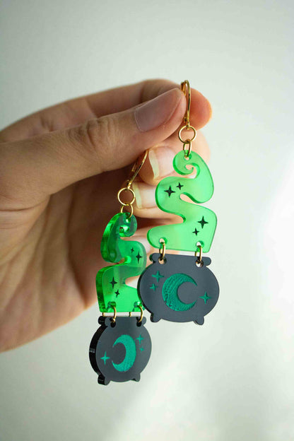 Paire de boucles d’oreilles chaudron magique tenue en main par les dormeuses dorées