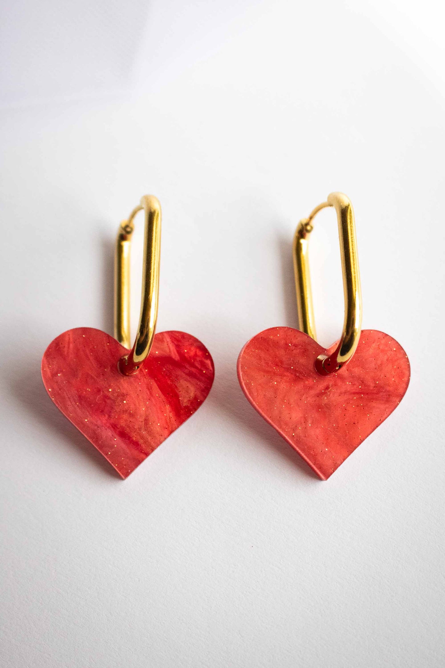 Paire de boucles pendantes cœur rouge marbré en acrylique découpé au laser, anneaux ovales plaqués or, fait main par Limonade Studio, fond blanc