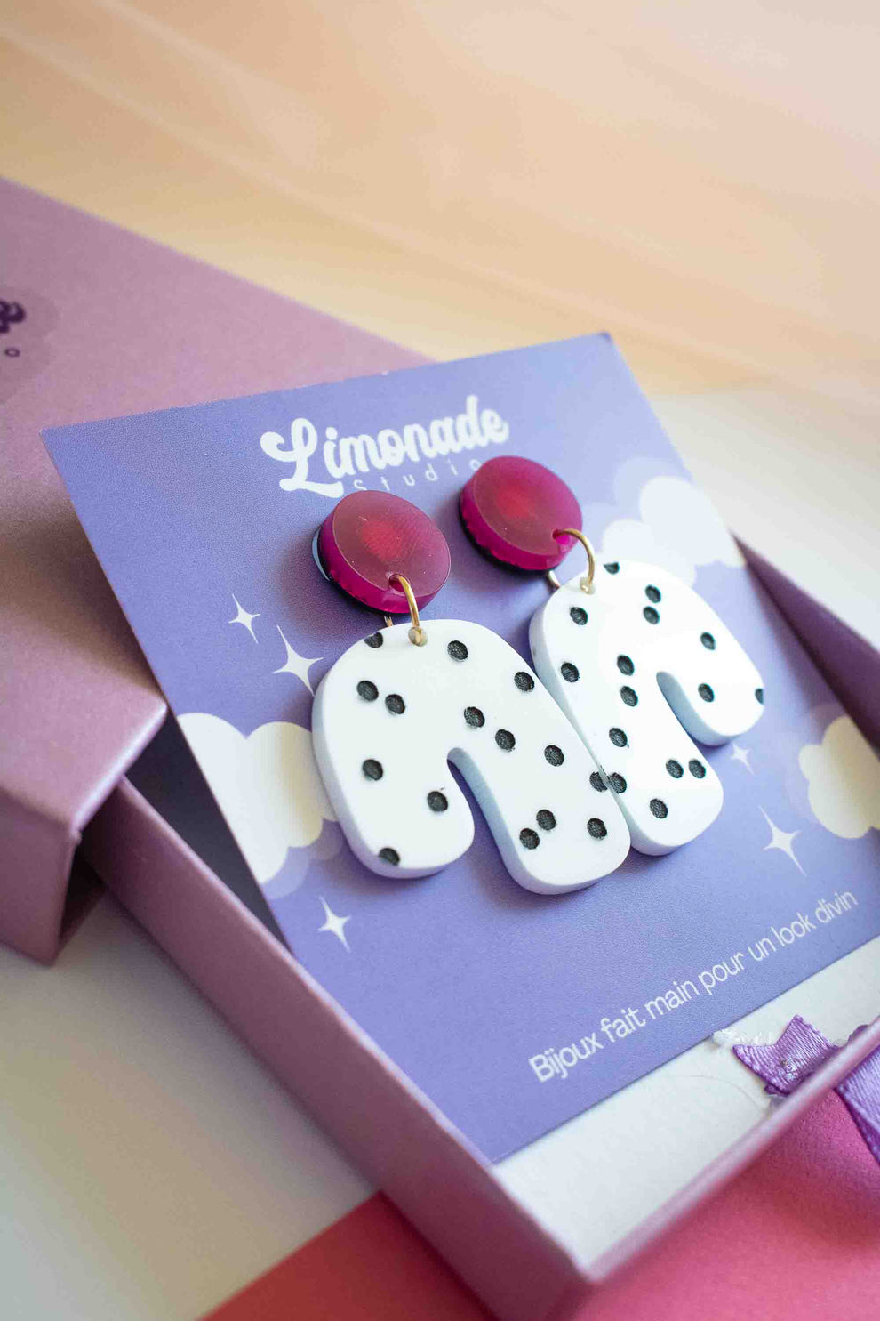 Boucles d'oreilles en acrylique rose et blanc à pois noirs, clou en acier inoxydable plaqué or 18 carats. Un bijou graphique signé Limonade Studio.