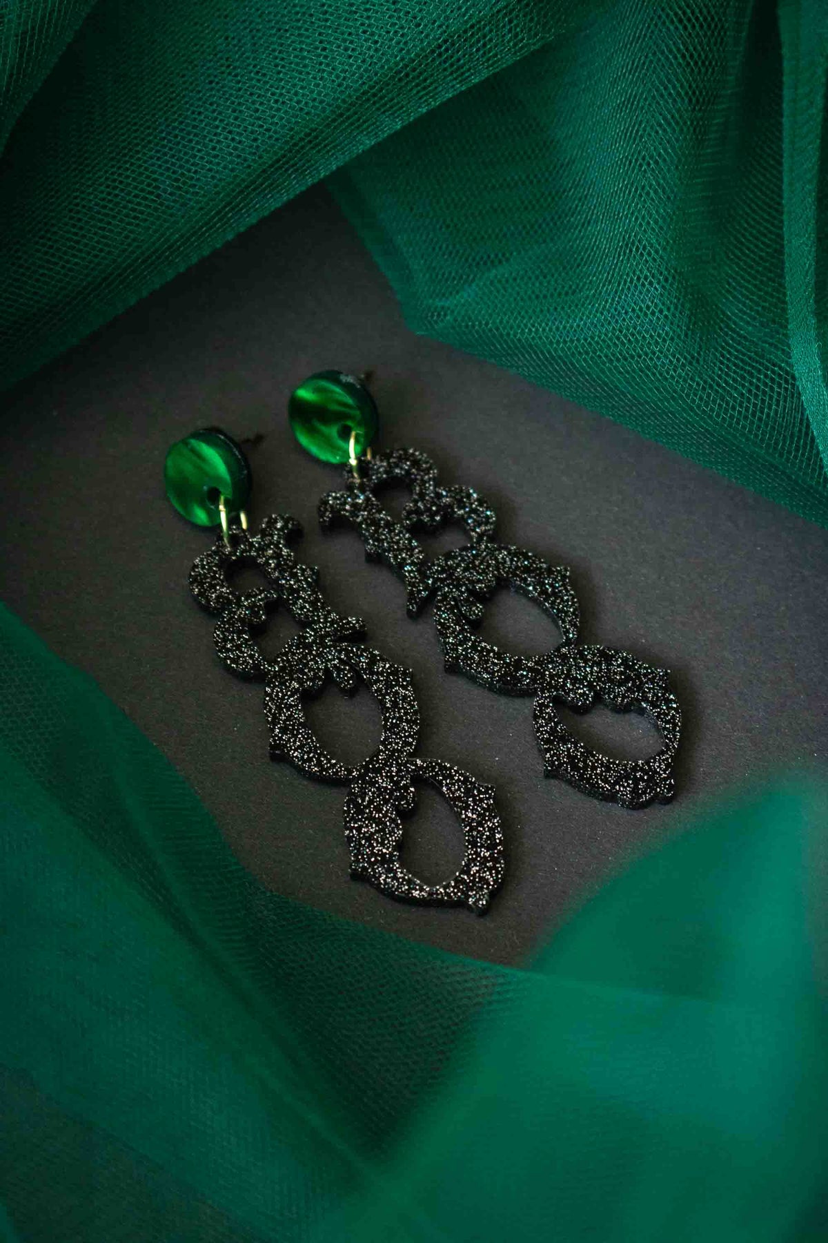 Boucles d’oreilles BOO mises en scène sur fond noir et tissu vert