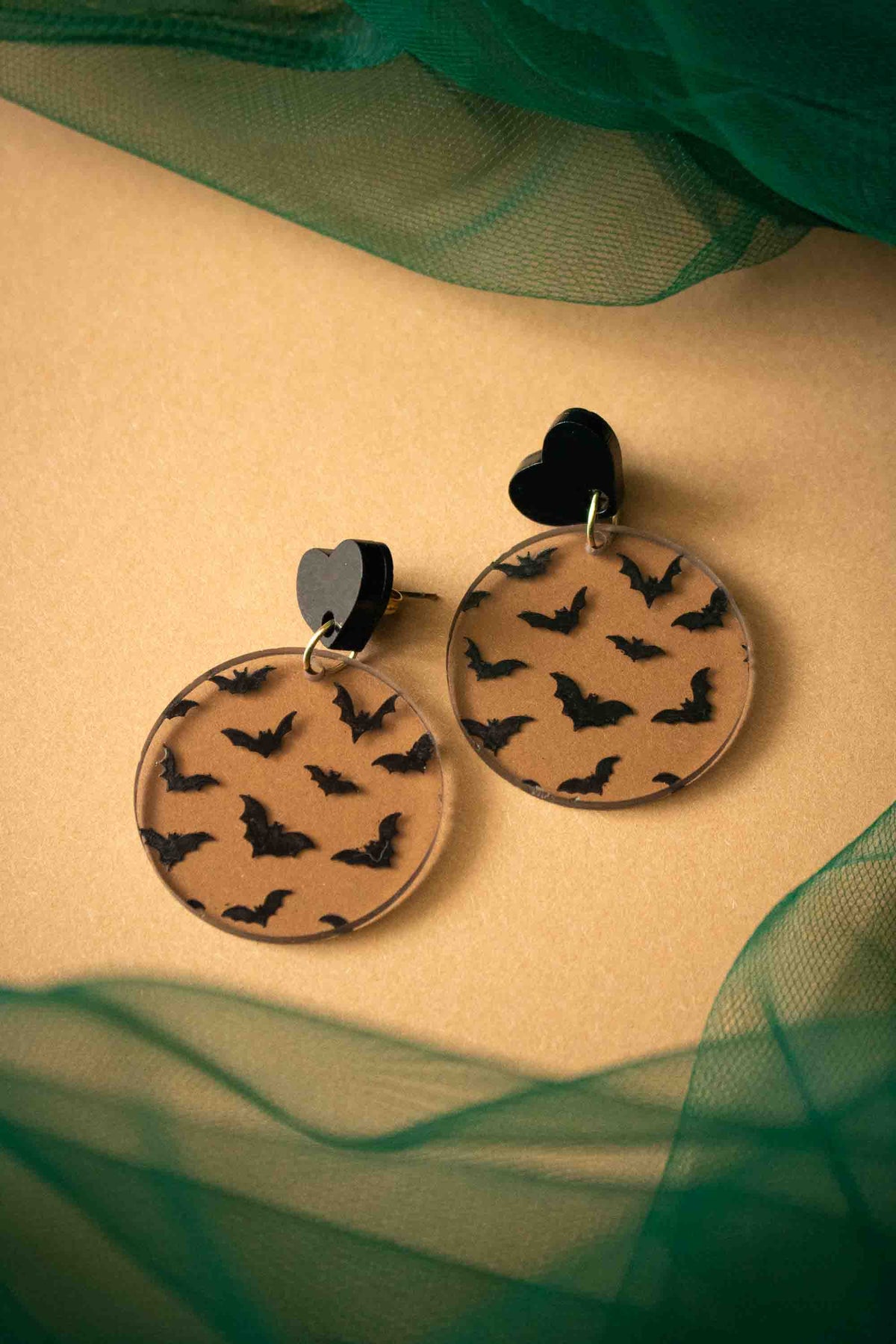 Boucles d’oreilles Halloween marron transparent et noir posées sur un voile vert