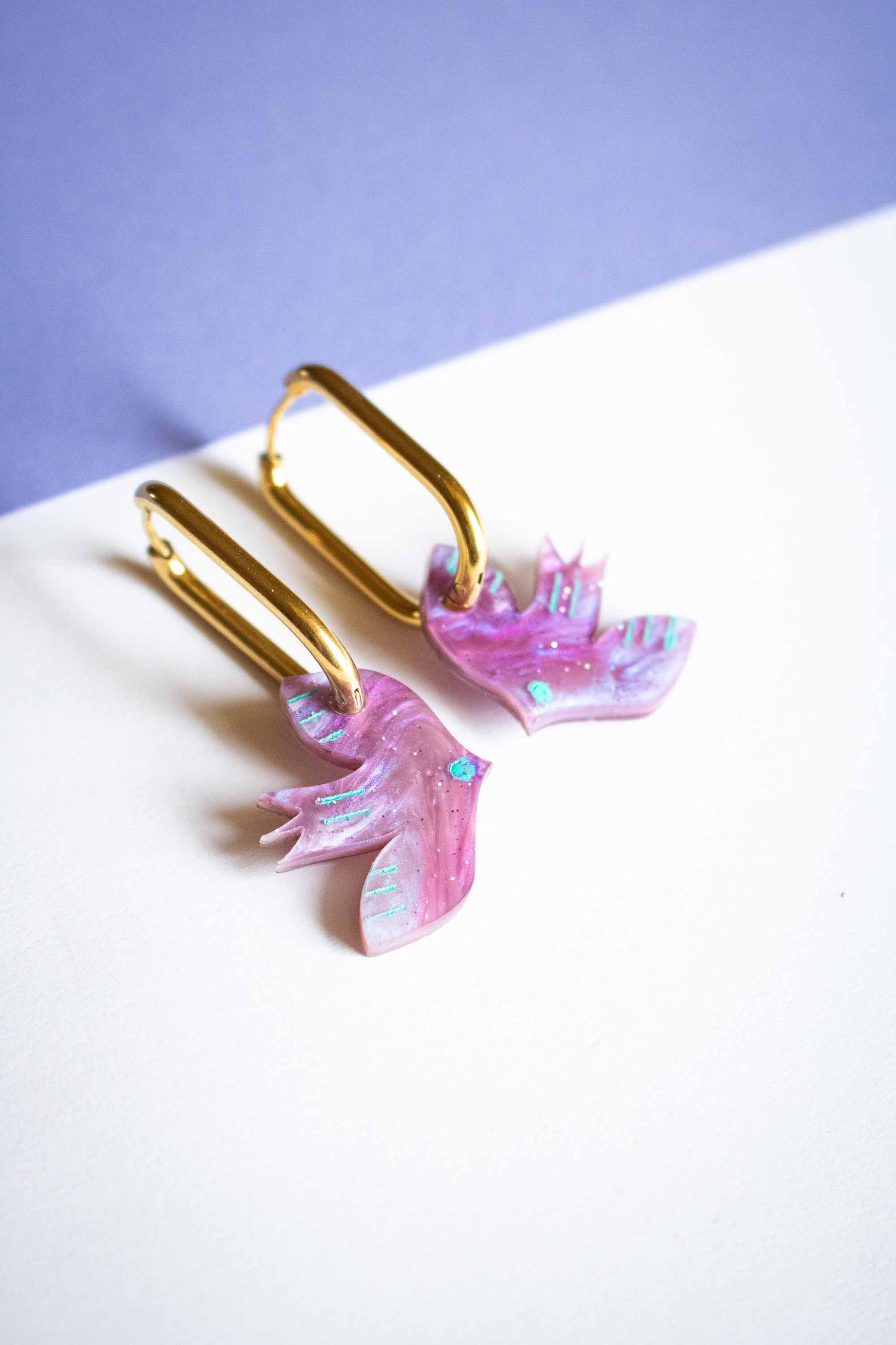 Paire de boucles d'oreilles oiseau violet géométrique, acrylique découpé laser, créateur français Limonade Studio, posées sur fond bicolore