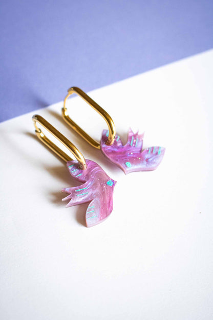 Paire de boucles d'oreilles oiseau violet géométrique, acrylique découpé laser, créateur français Limonade Studio, posées sur fond bicolore