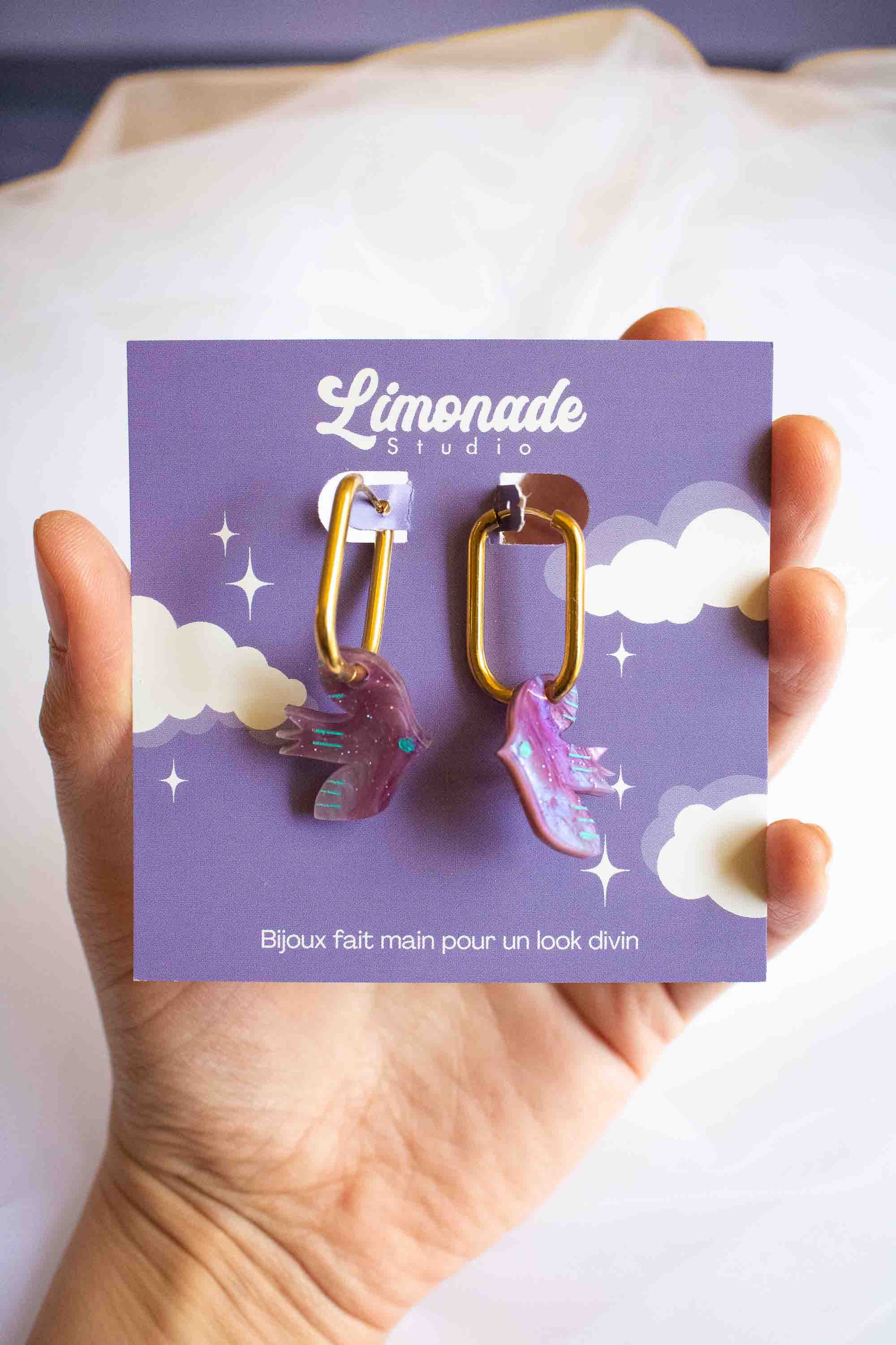 Boucles d'oreilles huggies oiseau violet en acrylique marbré, anneau acier doré, fait main par Limonade Studio, sur cartonnette tenue en main
