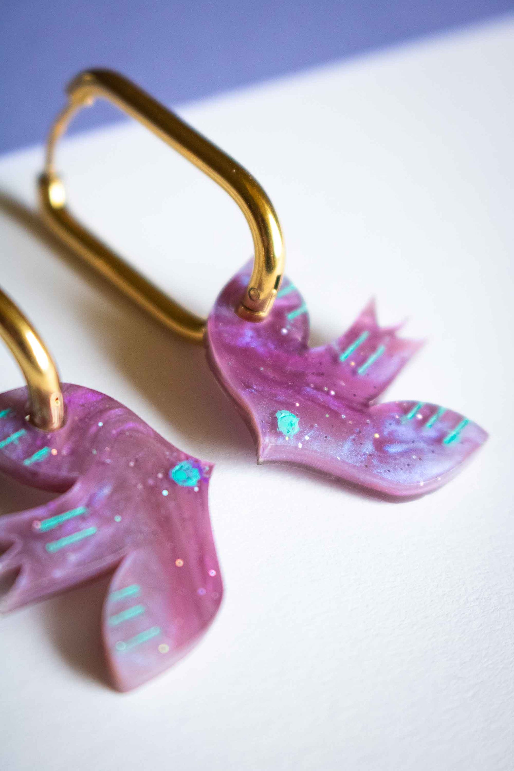 Gros plan boucles d'oreilles oiseau violet acrylique marbré rose et violet, accents turquoise peints, fait main Limonade Studio, détail macro