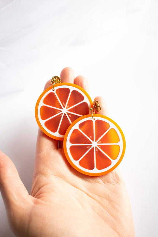 Boucles d'oreilles orange en acrylique découpé au laser, cadeau original artisanal, puce dorée plaquée or, Limonade Studio, posées dans la paume