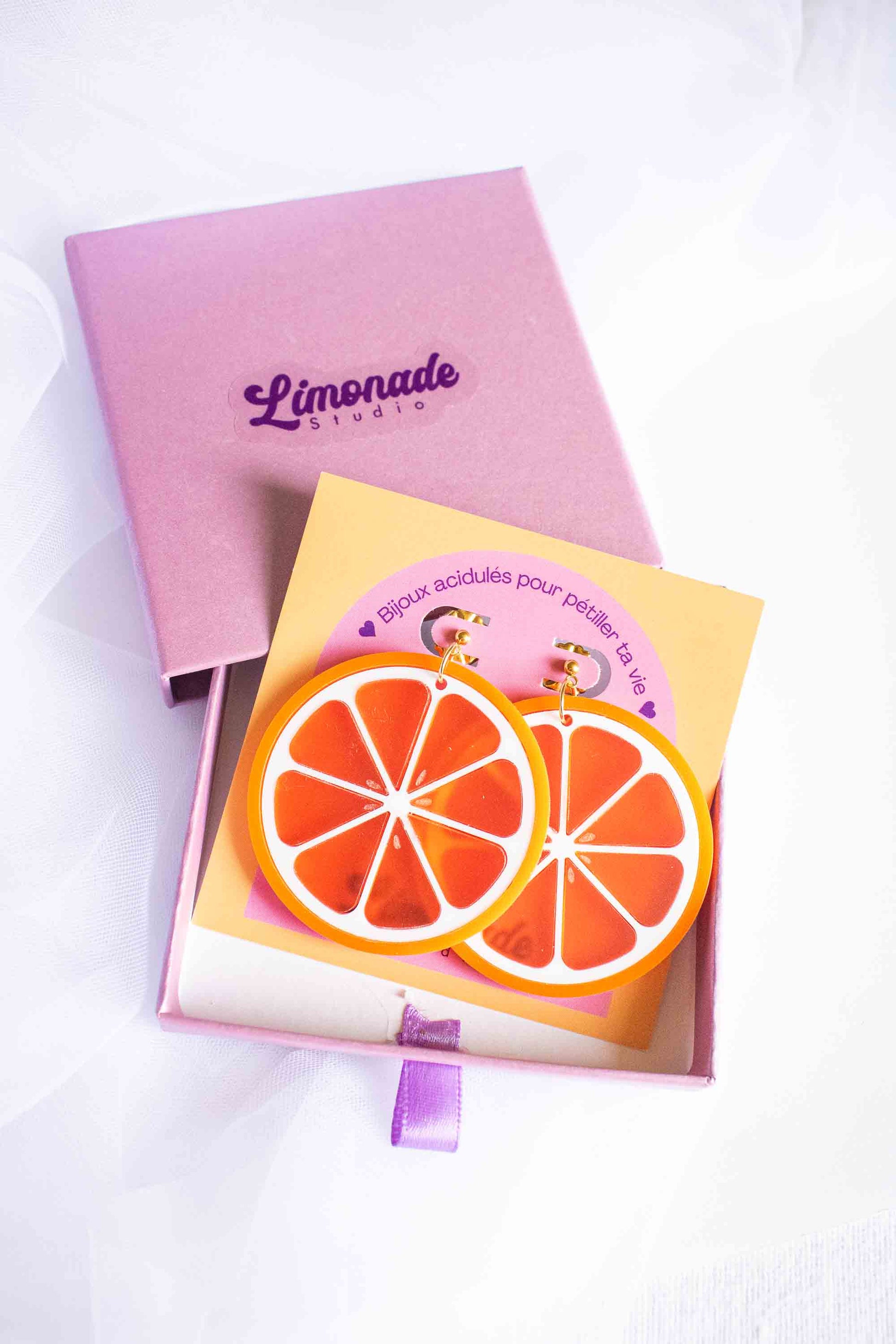 Boucles d'oreilles tranche d'orange artisanales en acrylique fait main, puce dorée, Limonade Studio, présentées sur cartonnette dans boîte cadeau violette