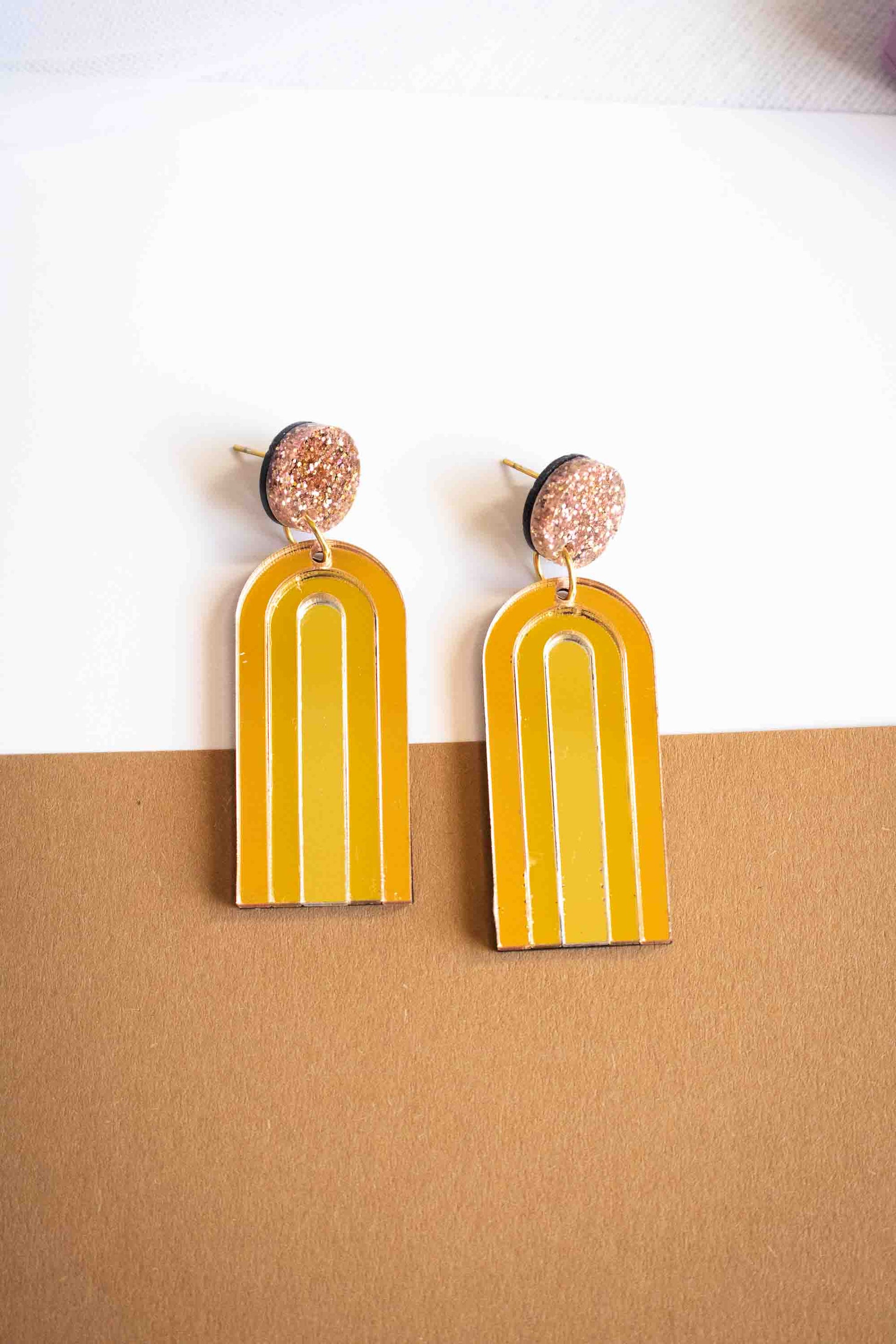 Paire de boucles d'oreilles pendantes arche jaune moutarde miroir, acrylique découpé au laser, fait main cadeau femme, Limonade Studio, sur fond caramel