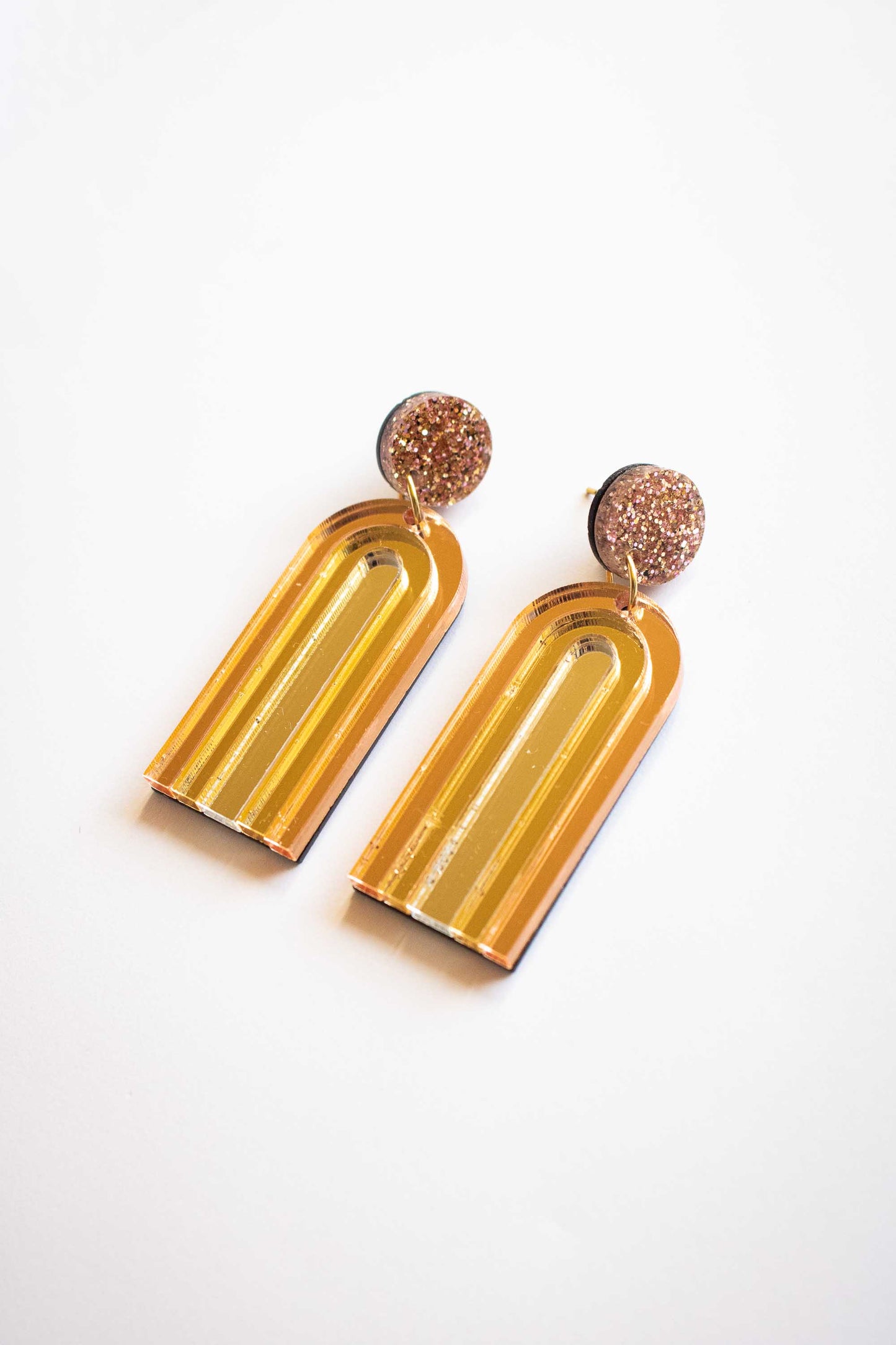 Boucles d'oreilles pendantes arche or miroir en acrylique découpé au laser, bijou fantaisie fait main, Limonade Studio, posées sur fond blanc