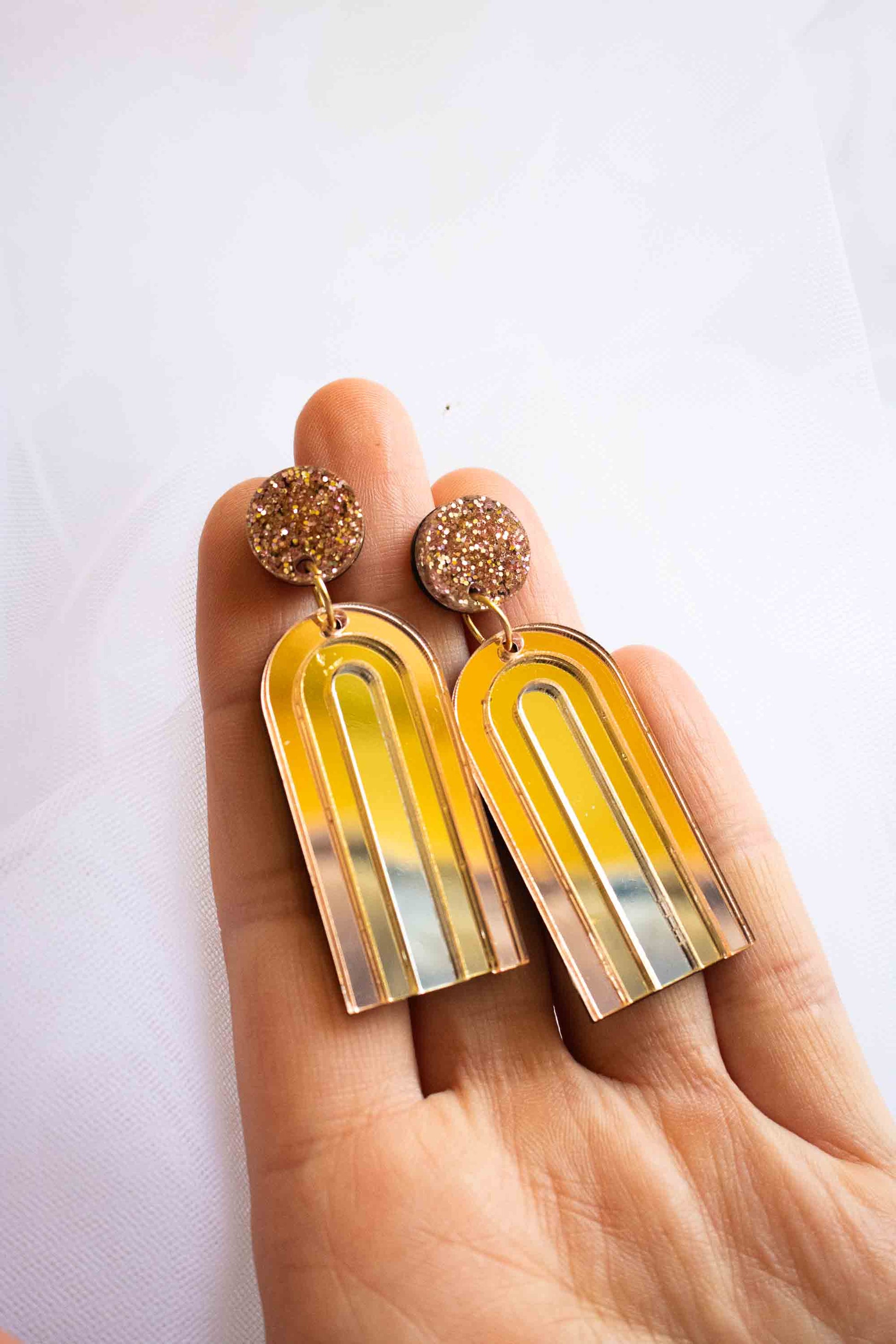 Boucles d'oreilles pendantes arche or miroir en acrylique découpé au laser, puce pailletée rose gold, fait main Limonade Studio, tenues en paume de main