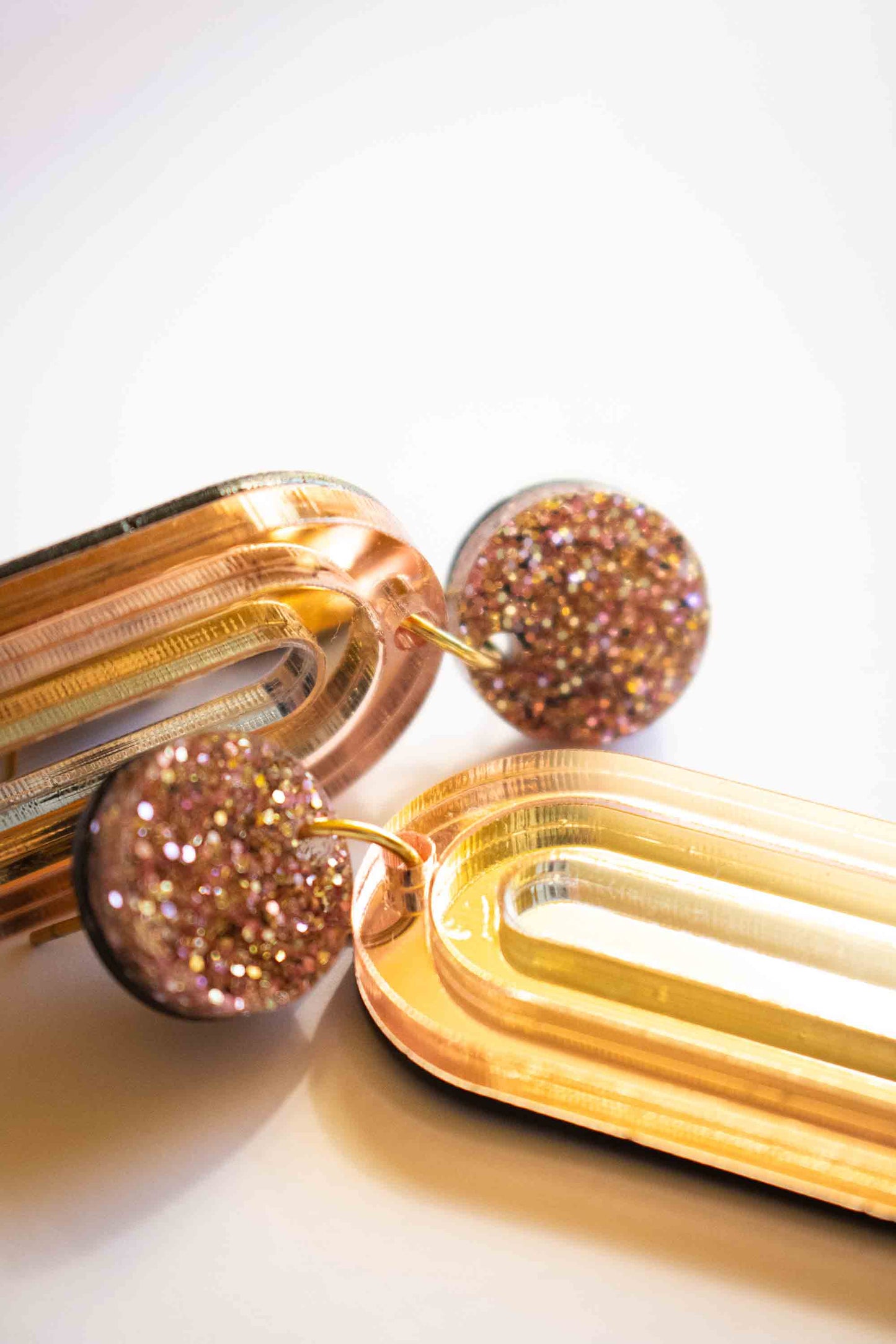 Gros plan texture boucles d'oreilles pendantes arche or miroir et puce pailletée rose gold, acrylique découpé au laser, fait main Limonade Studio