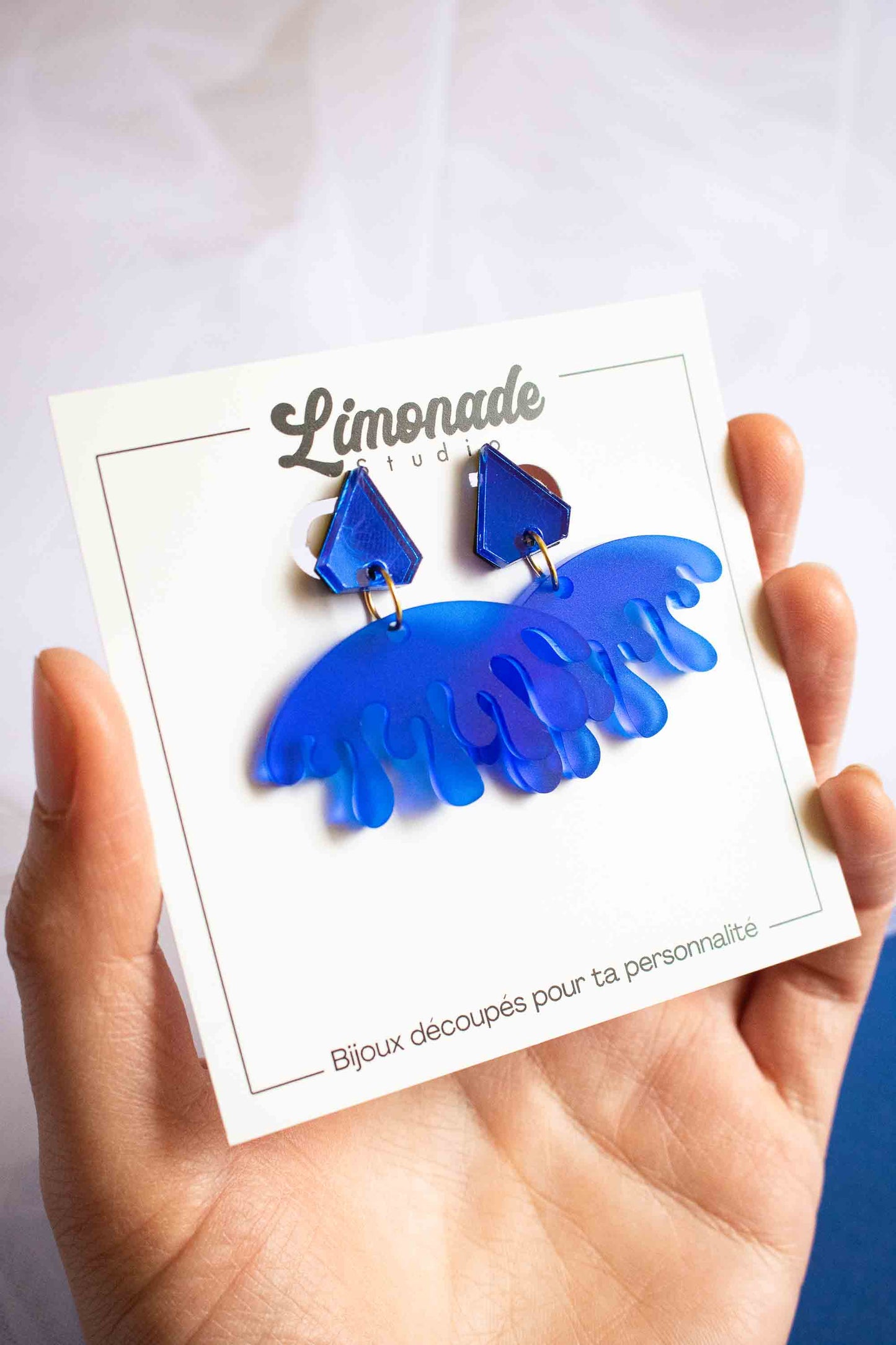 Boucles d'oreilles pendantes bleues acrylique dépoli et miroir, bijou créateur fait main, Limonade Studio, cartonnette tenue en main