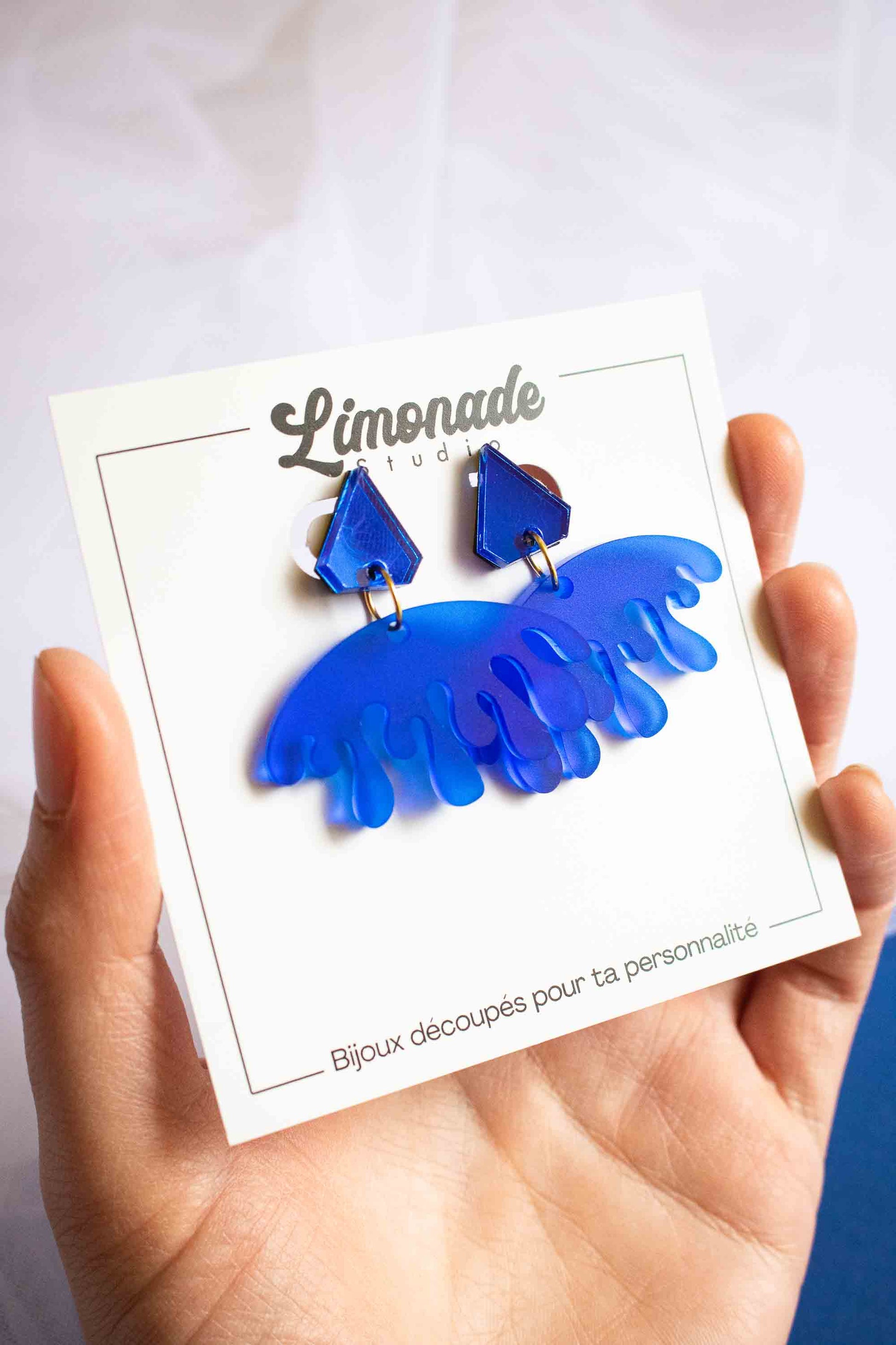 Boucles d'oreilles pendantes bleues acrylique dépoli et miroir, bijou créateur fait main, Limonade Studio, cartonnette tenue en main