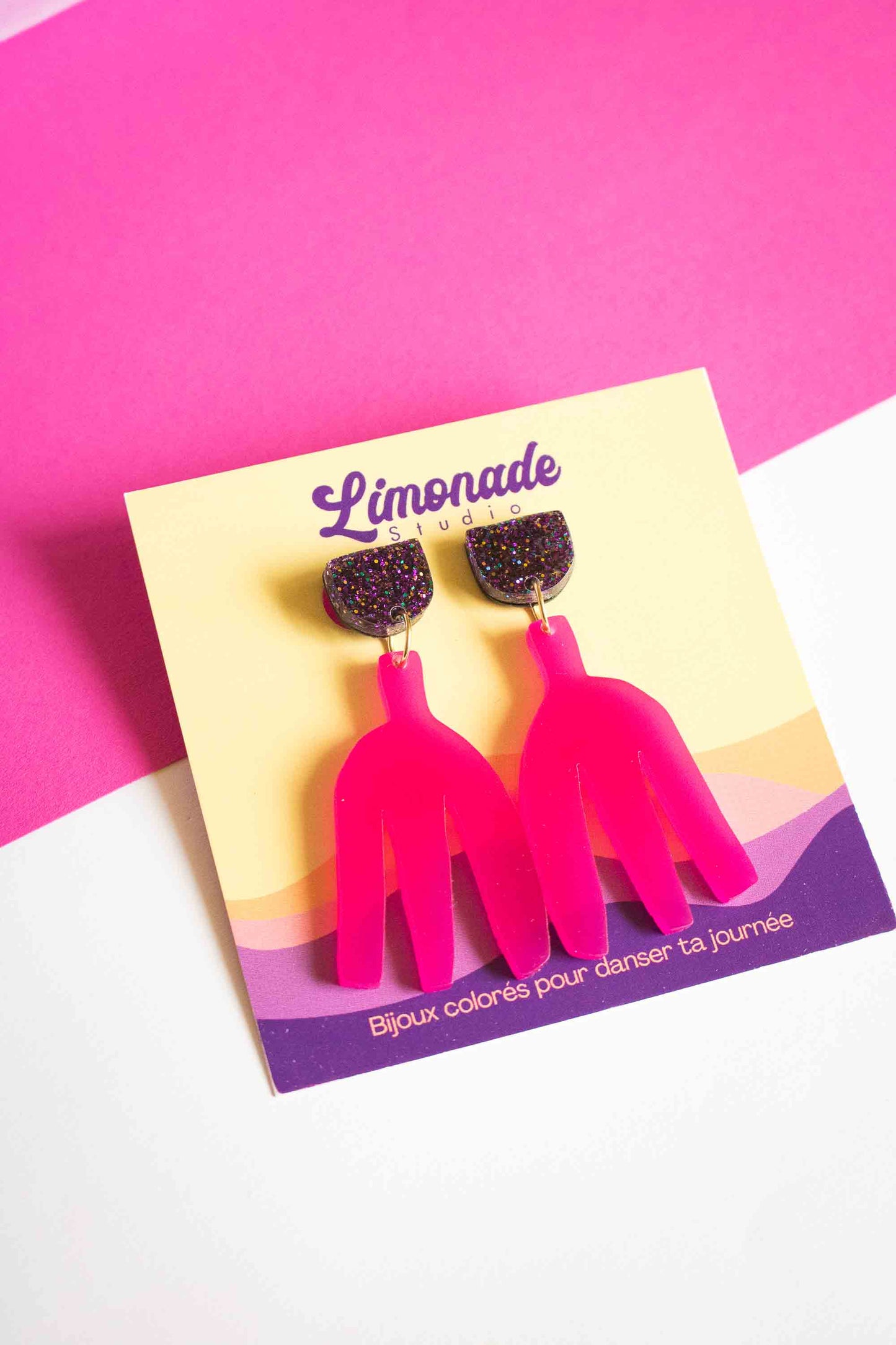 Boucles d'oreilles pendantes fuchsia acrylique laser sur cartonnette Limonade Studio, fond bicolore rose et blanc, cadrage serré