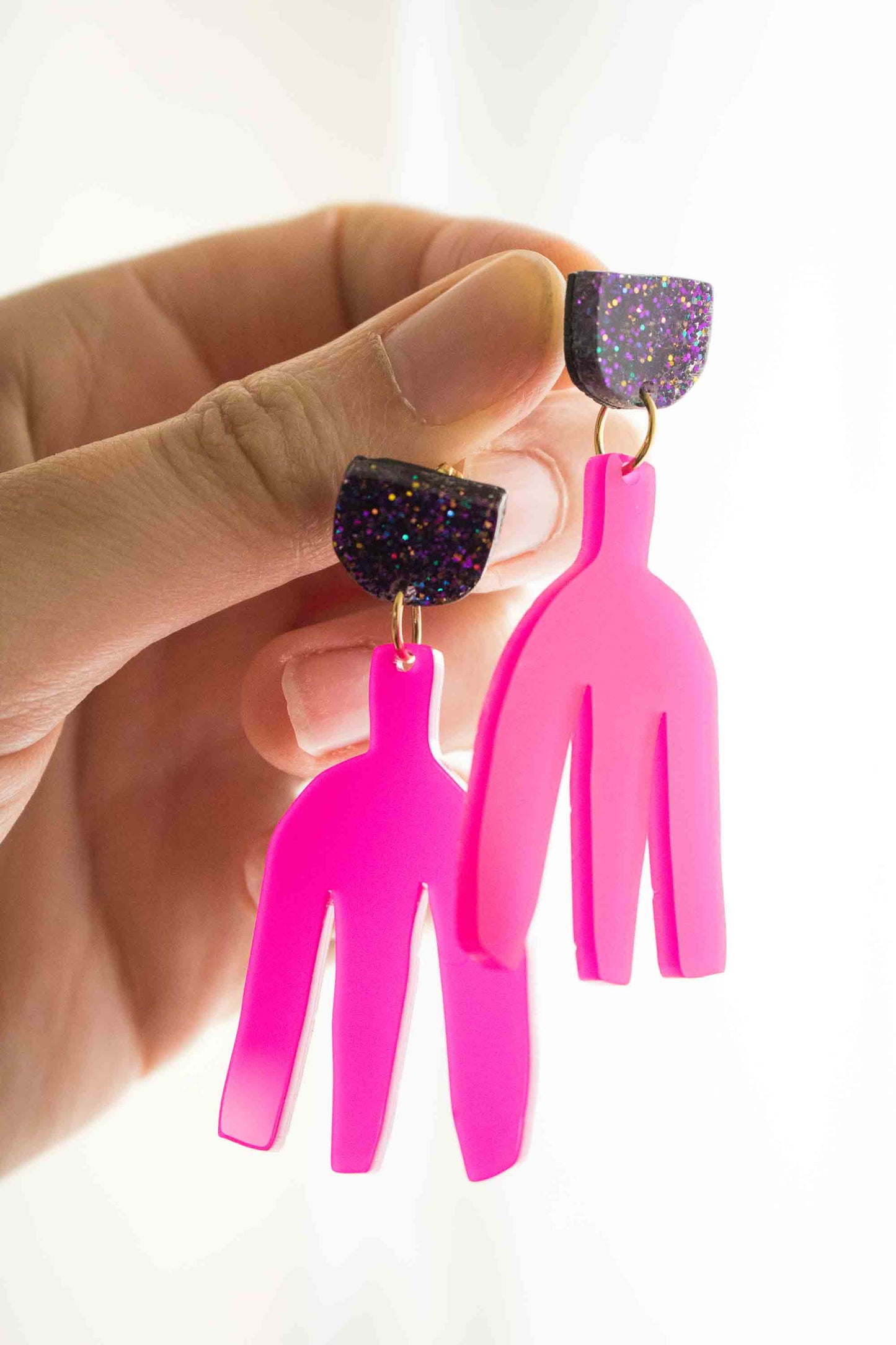 Boucles pendantes fuchsia acrylique laser tenues entre les doigts, vue de profil, détail de la forme et de l'épaisseur