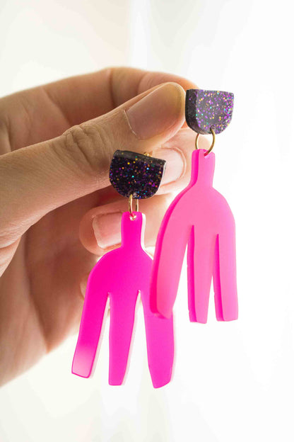 Boucles pendantes fuchsia acrylique laser tenues entre les doigts, vue de profil, détail de la forme et de l'épaisseur