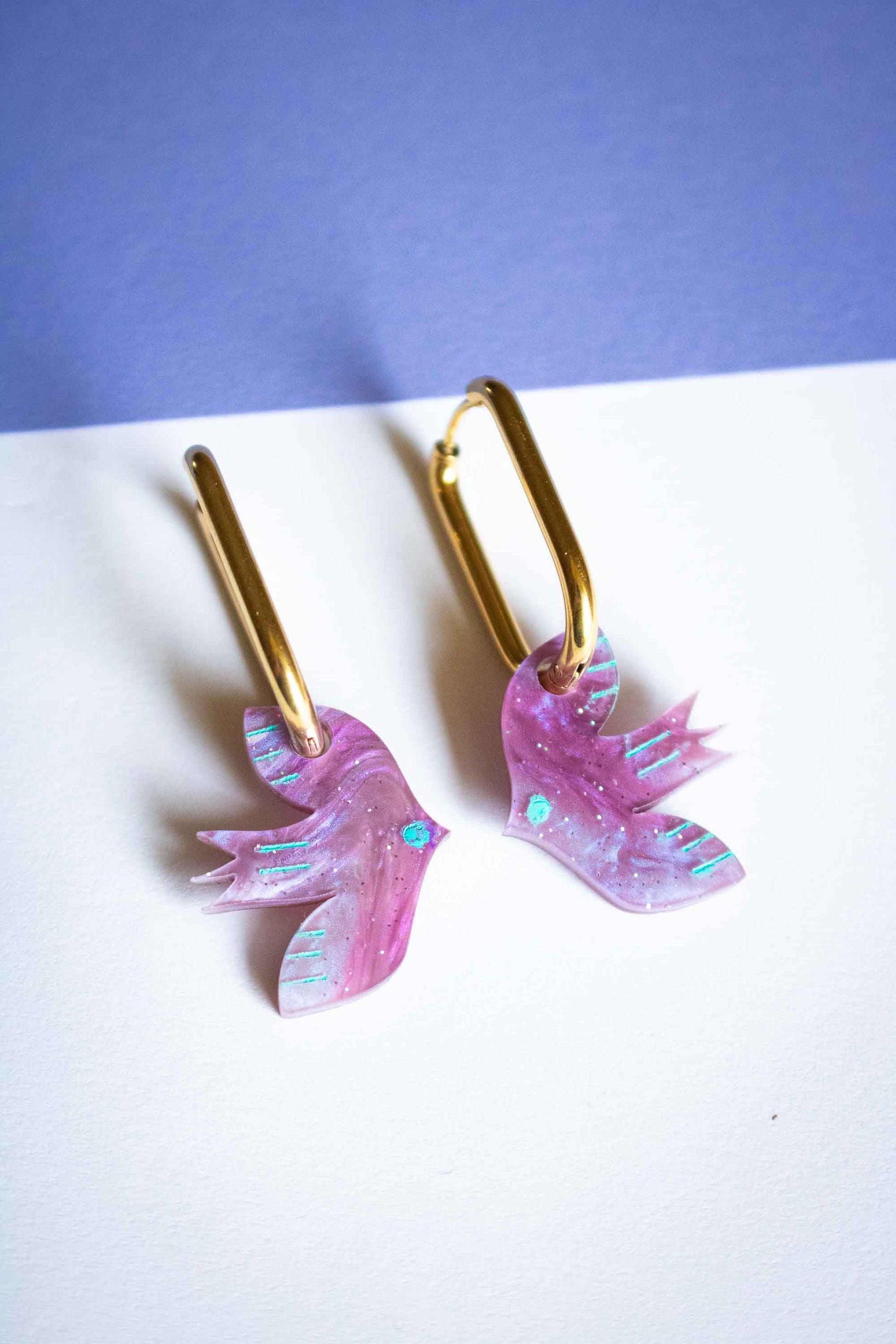 Paire de boucles d'oreilles oiseau violet géométrique, acrylique découpé laser, créateur français Limonade Studio, posées sur fond bicolore