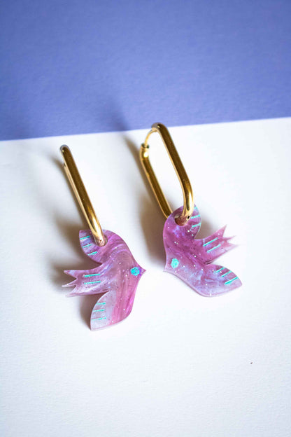 Paire de boucles d'oreilles oiseau violet géométrique, acrylique découpé laser, créateur français Limonade Studio, posées sur fond bicolore
