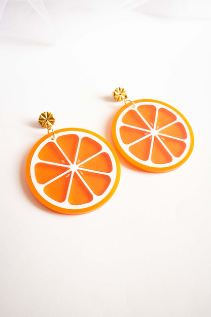 Paire de boucles d'oreilles pendantes orange en acrylique découpé au laser, bijou coloré artisanal, puce dorée, Limonade Studio, vue posée décalée