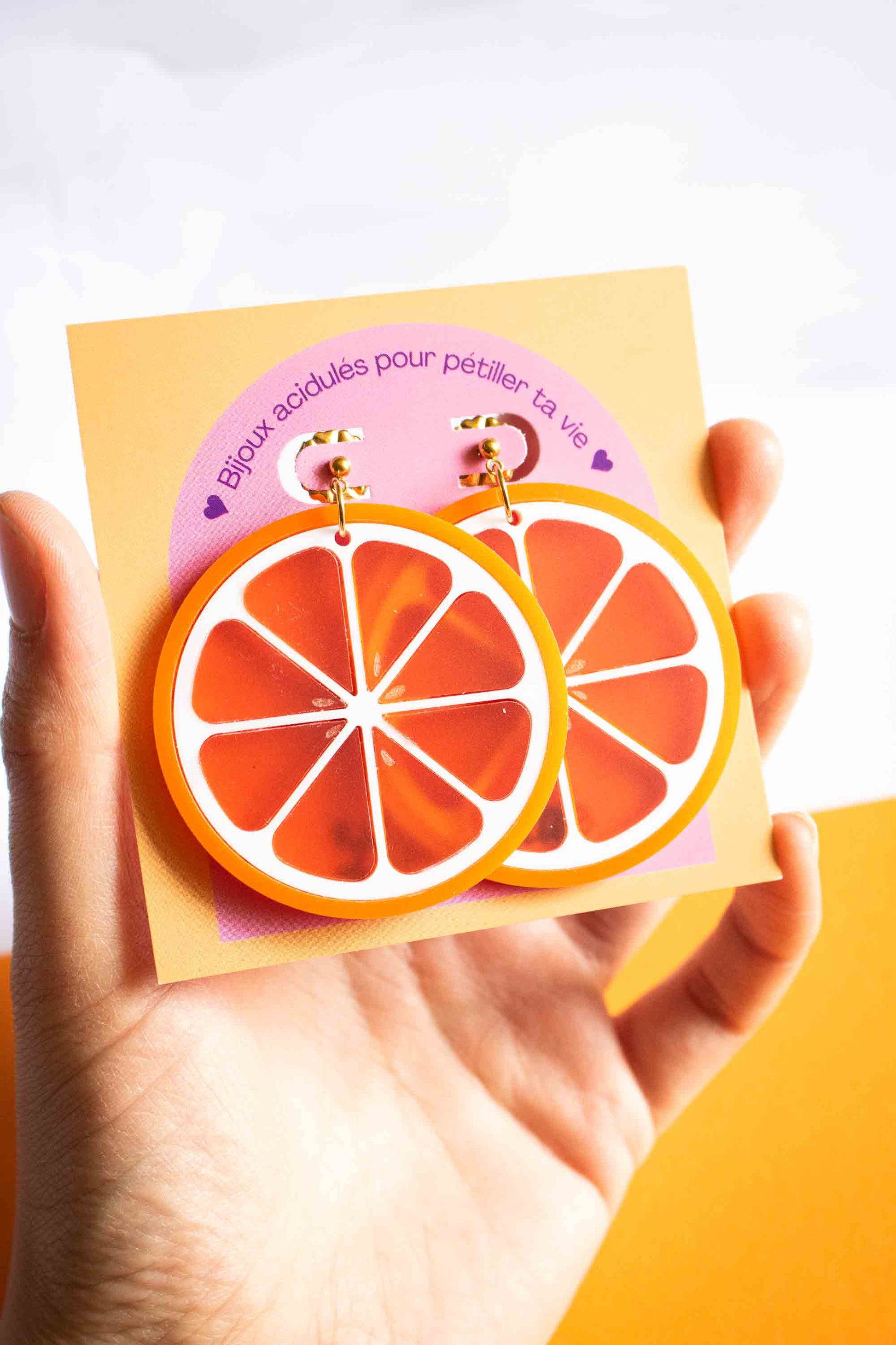 Boucles d'oreilles orange acidulé en acrylique découpé au laser, cadeau original bijou fantaisie, Limonade Studio, sur cartonnette tenue en main
