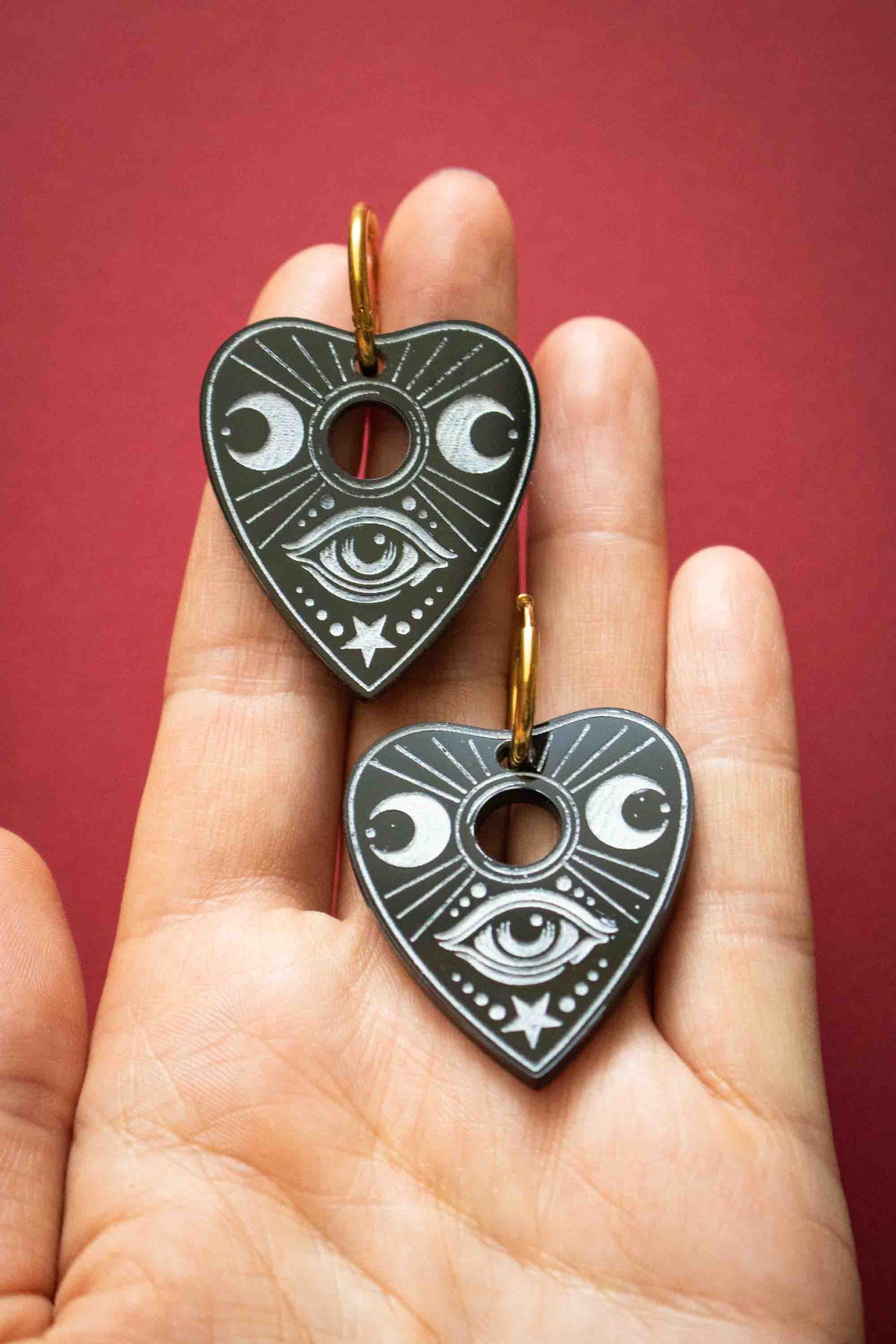 Paire de boucles Ouija noires posée dans une main pour visualiser leurs dimensions réelles